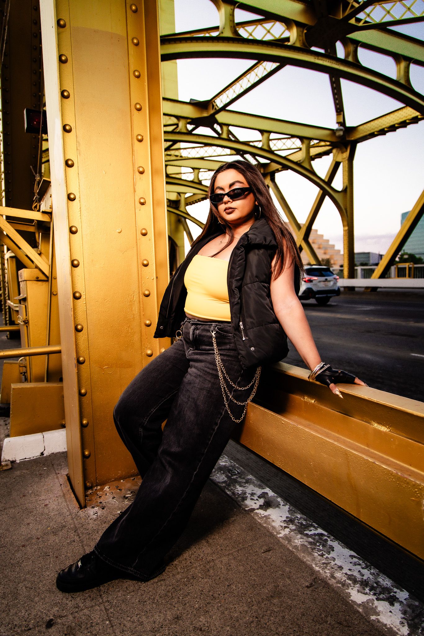 Fashion portrait in black dress against golden architectural bridge structure interior creates dramatic urban contrast.
