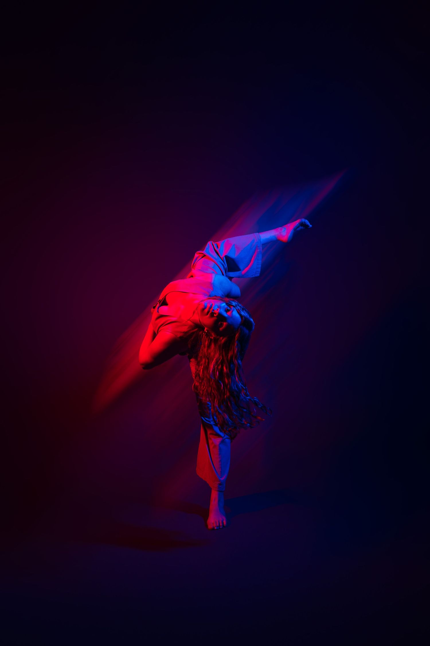 Abstract dance movement captured in red and blue lighting against dark background showing flowing motion sequence.