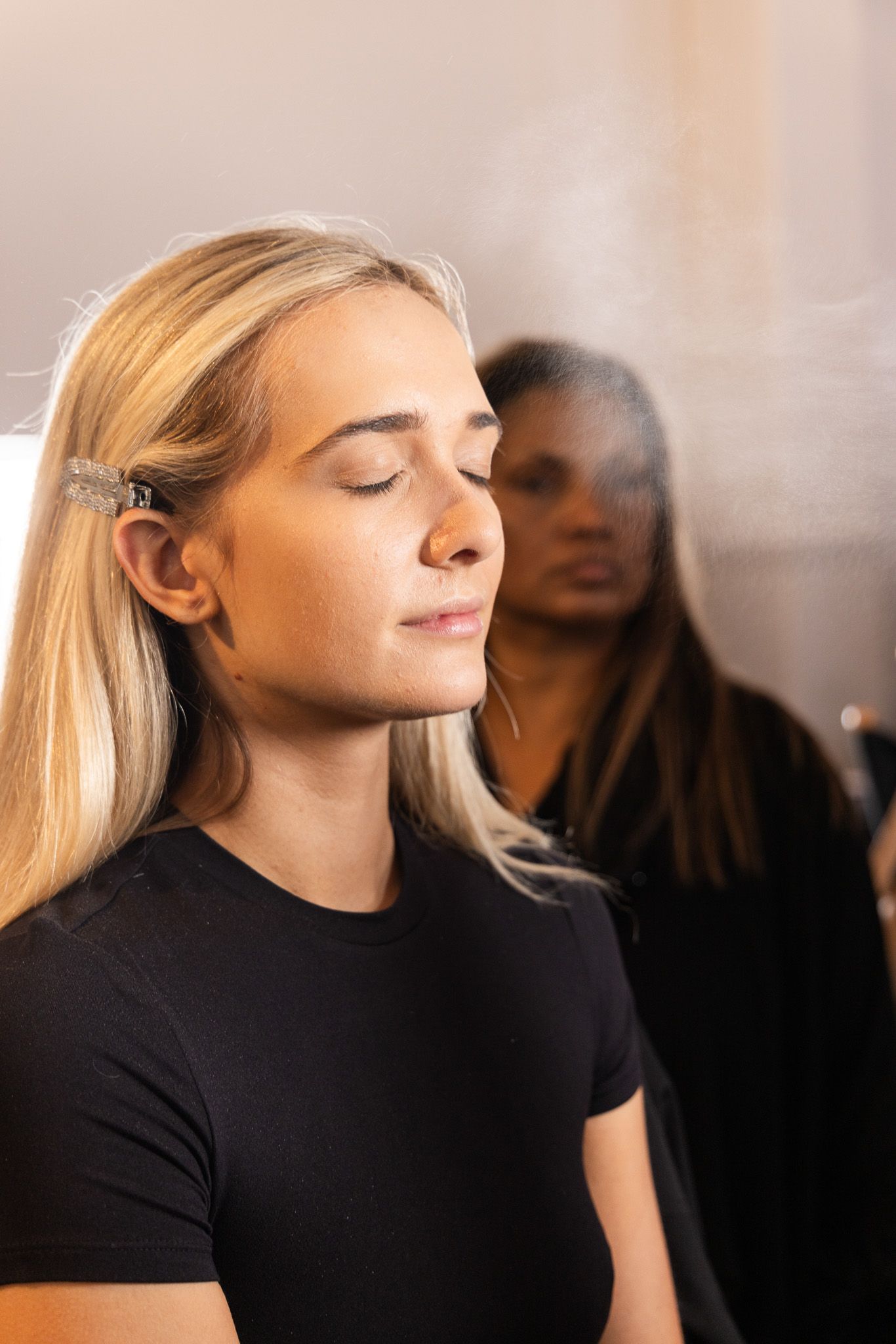 Woman in black shirt closes eyes peacefully while sitting against blurred background.