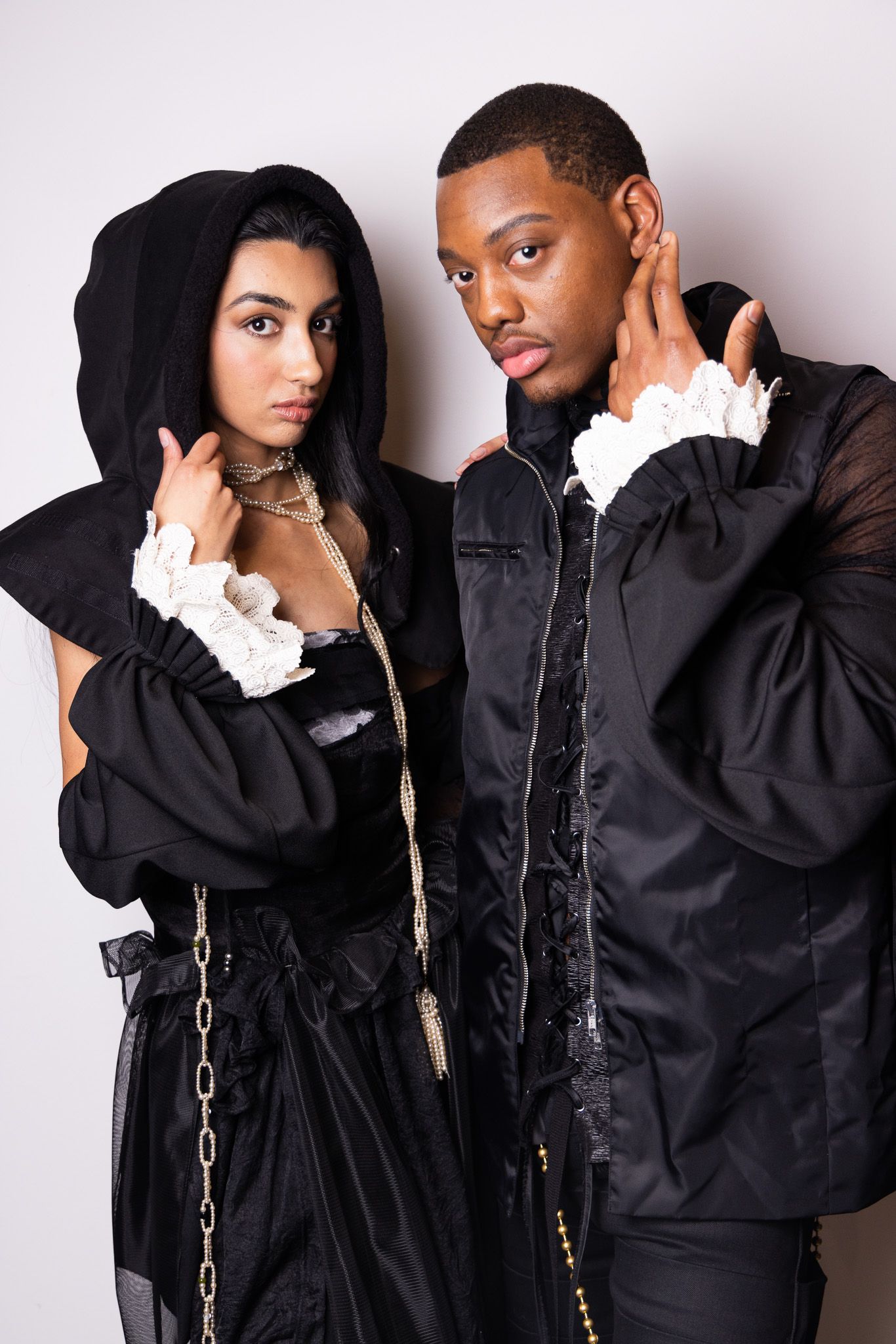 Fashion editorial with models in black hooded outfits against white background.