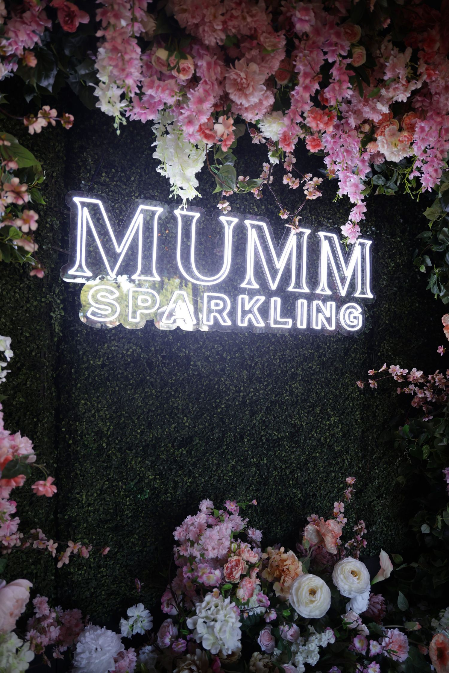 Illuminated 'MUMM SPARKLING' neon sign surrounded by pink and white floral decorations.