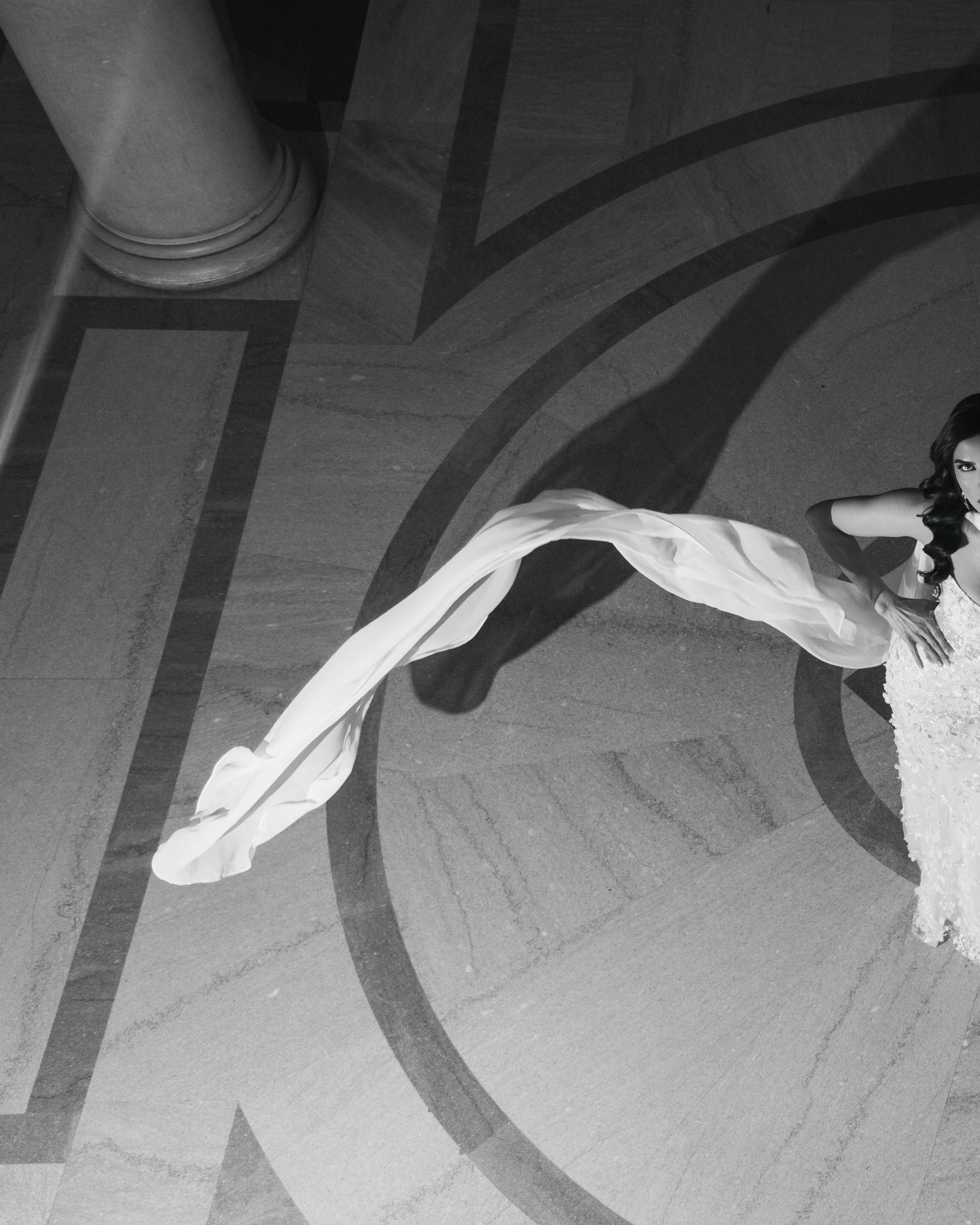 A dancer in white performs an elegant movement with flowing fabric creating graceful lines in black and white.