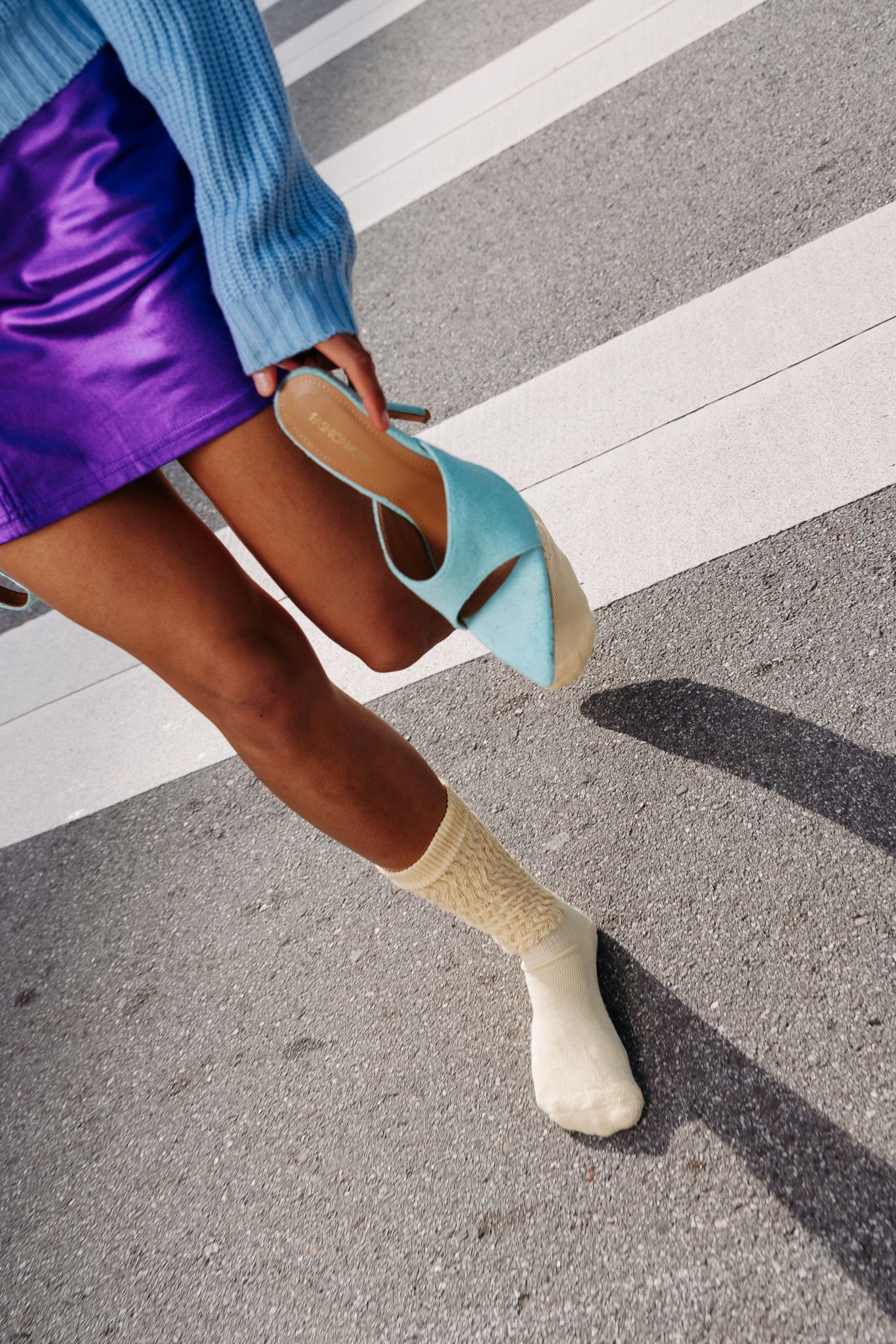 Close-up sequence of feet wearing light blue sweater, purple skirt and turquoise heels walking across zebra crossing.