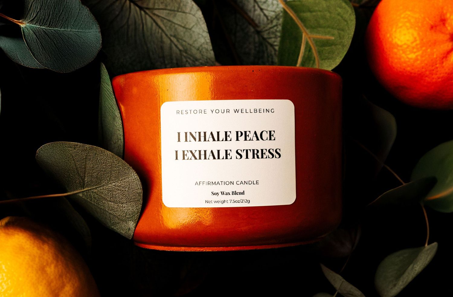 Orange scented candle with 'Inhale Peace Exhale Stress' text surrounded by green leaves and citrus fruits.