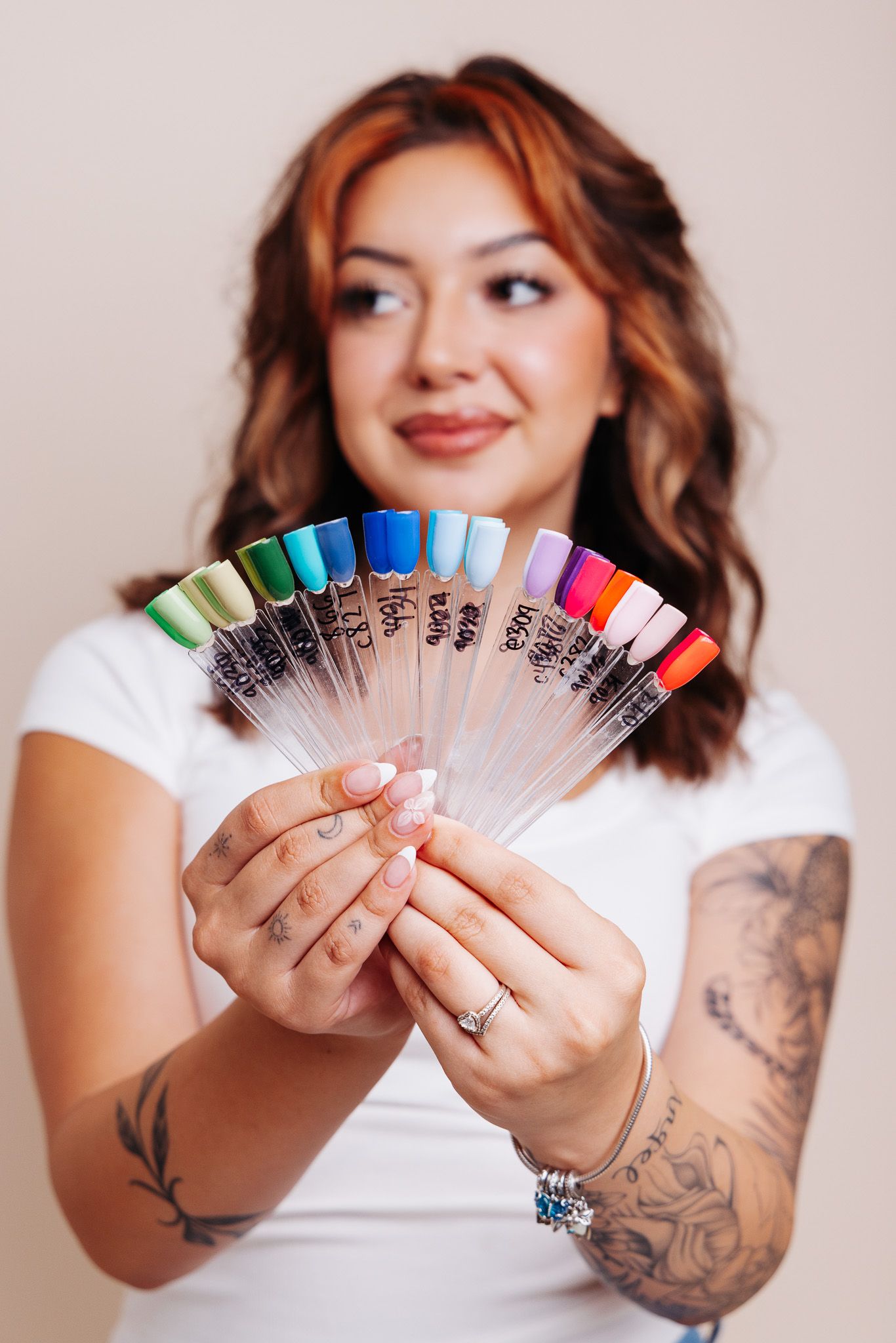 Woman with tattoos holding a fan of colorful nail polish swatches, showcasing a wide range of vibrant nail color options.