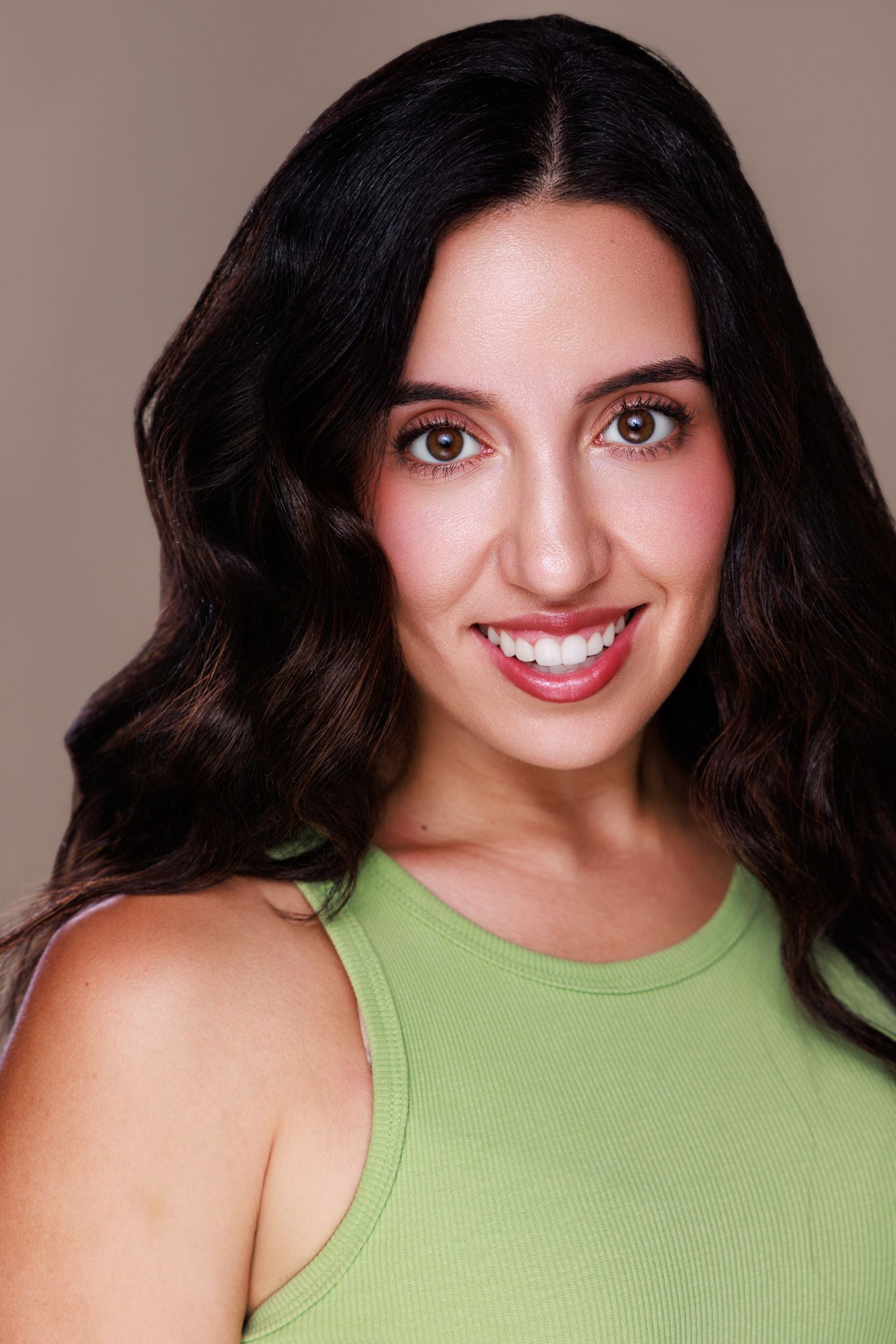 Young woman with dark wavy hair smiling, wearing a green sleeveless top, professional headshot photo.