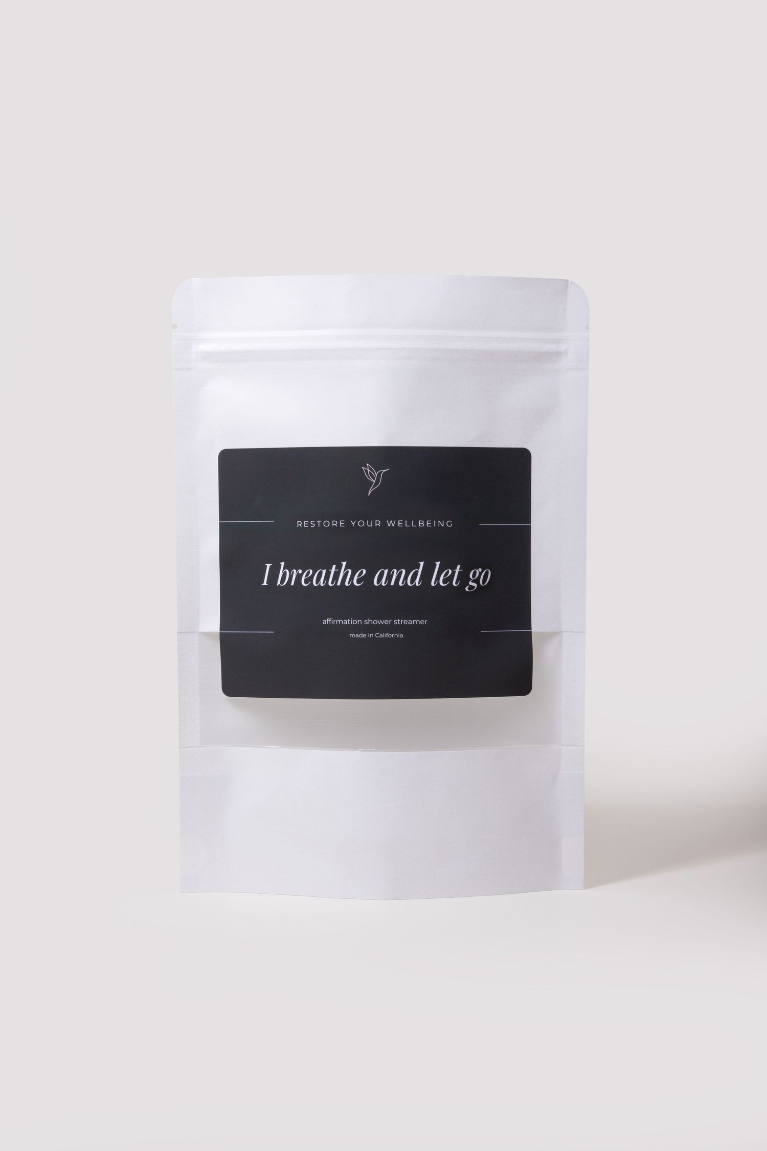 White pouch of Restore Your Wellbeing affirmation shower steamer labeled I Breathe and Let Go.