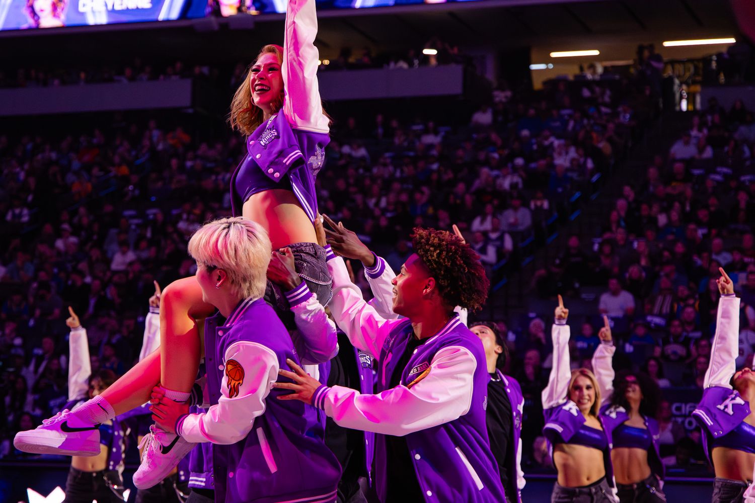 Cheerleaders perform dramatic lift stunt in purple jackets during NBA halftime show performance.