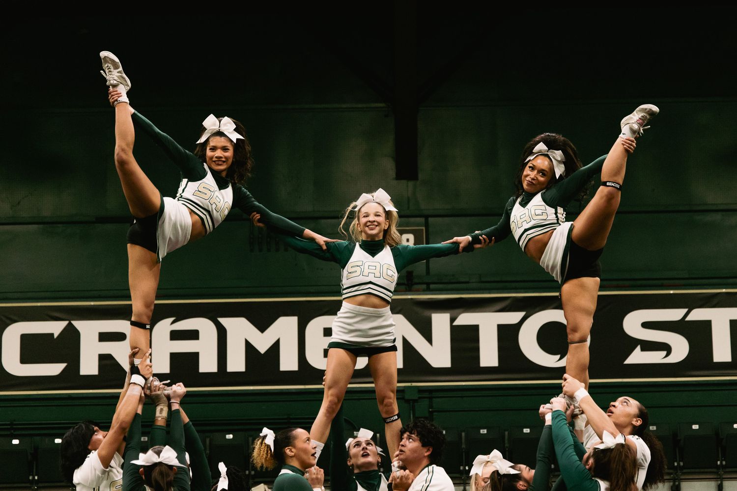 Sacramento State cheerleaders performing a high-flying stunt routine with flyers executing splits in the air.
