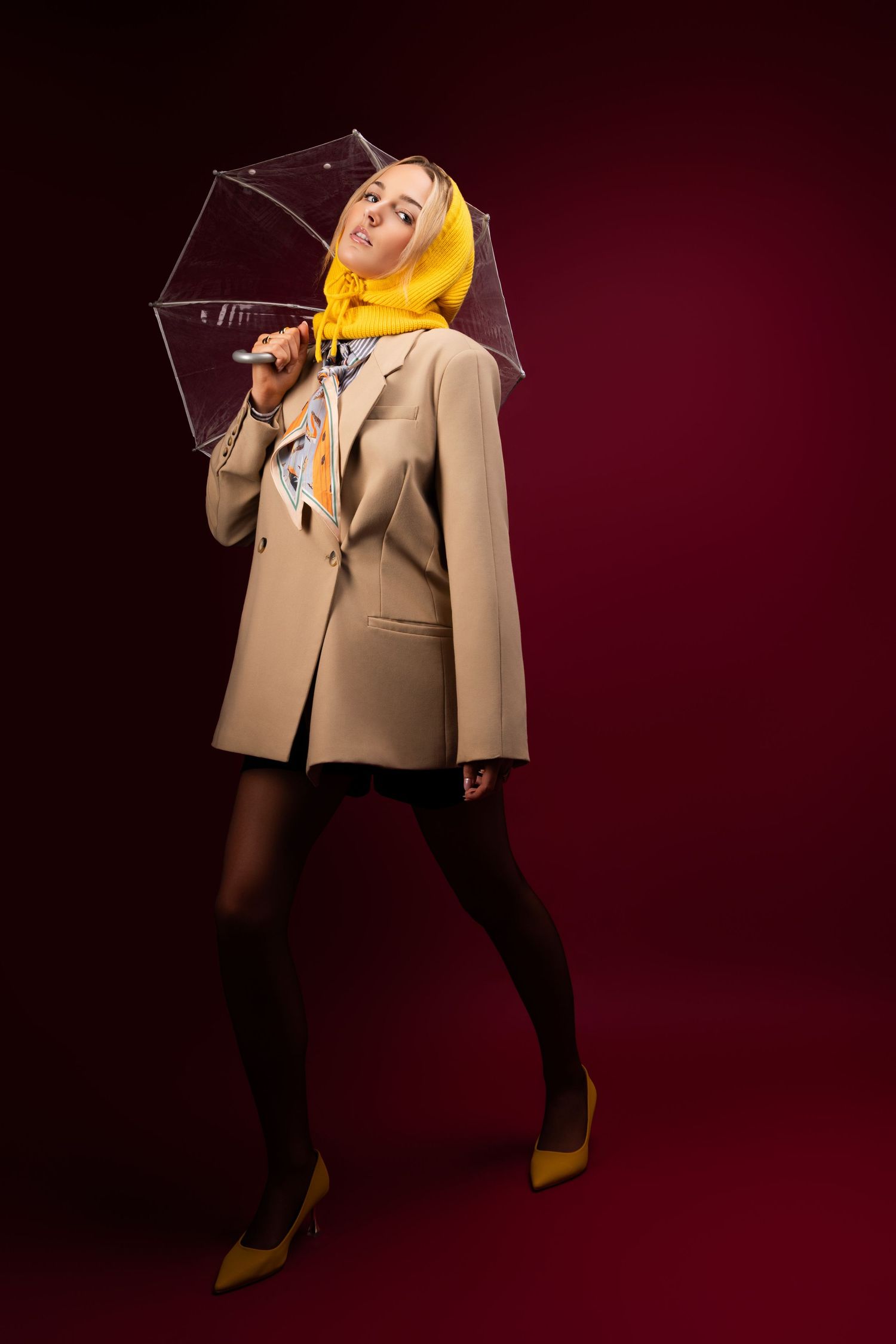 A performer in a beige blazer and black pants strikes dynamic poses against a dark red backdrop during a photoshoot.