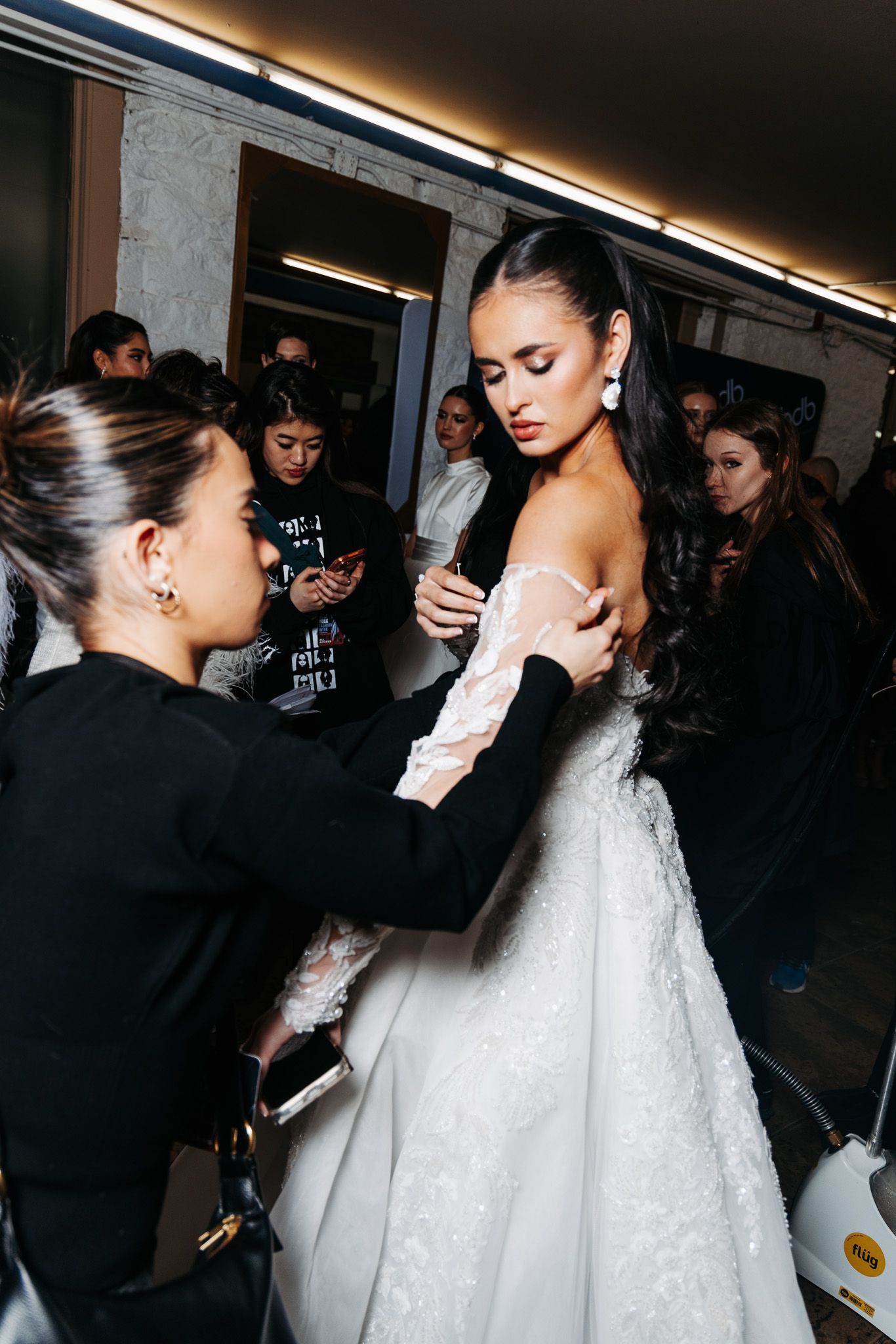 Behind-the-scenes fashion preparation showing stylists working on adjusting a white dress.