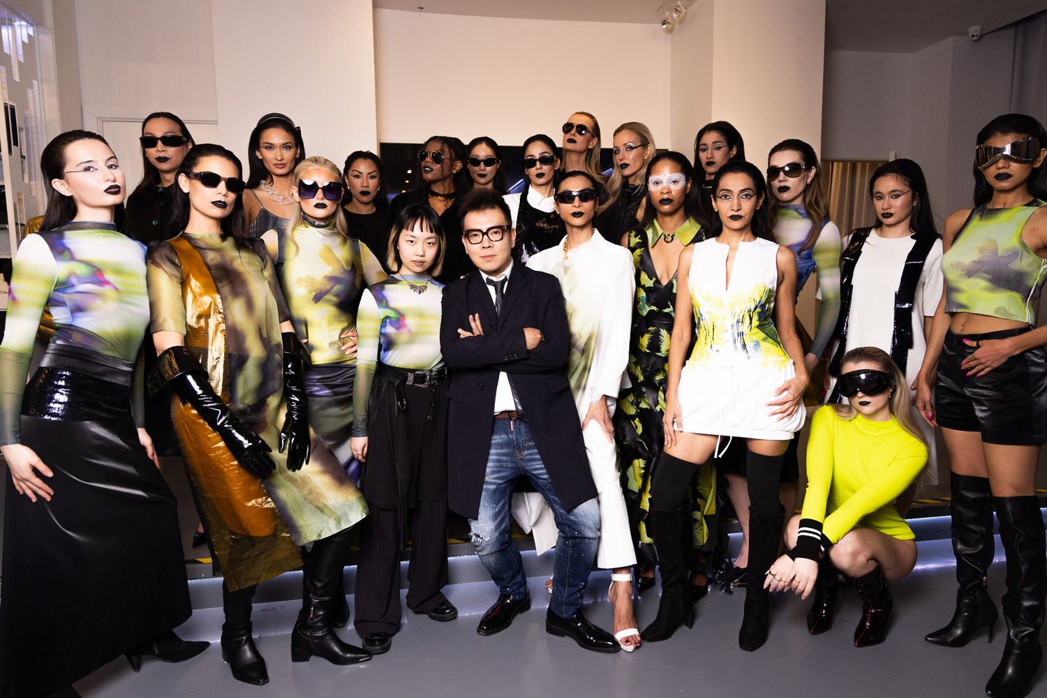 Large group of fashion models and attendees posing together at a stylish event against a white backdrop.