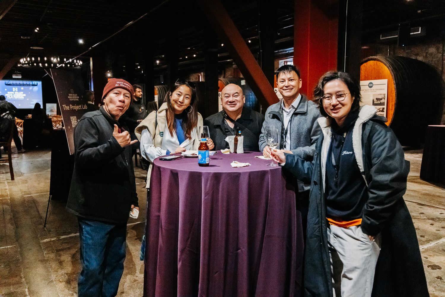 Event guests mingle around cocktail tables during a reception with purple tablecloths.