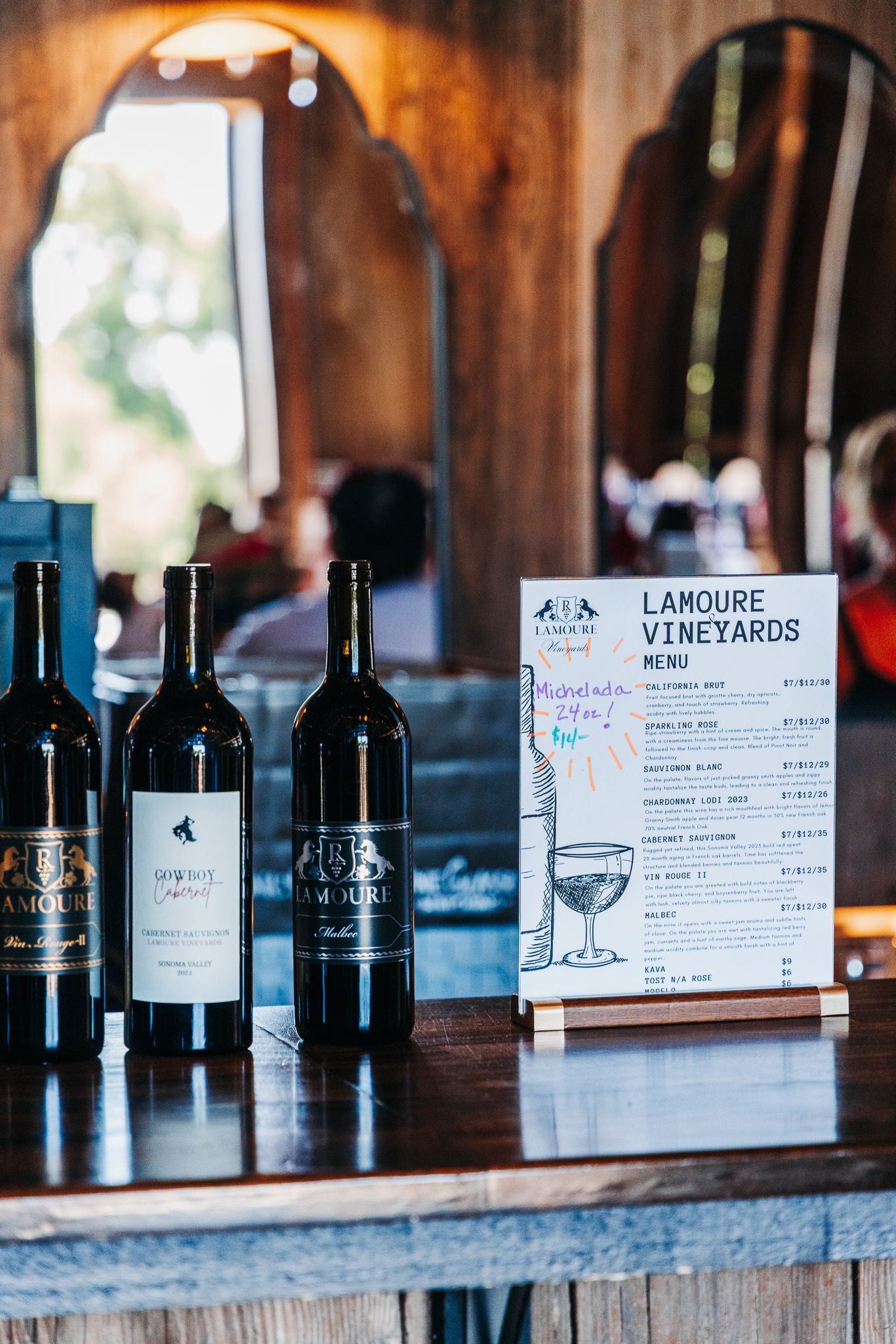 LaMoure Vineyards wine menu display with three red wine bottles on a rustic wooden bar counter.