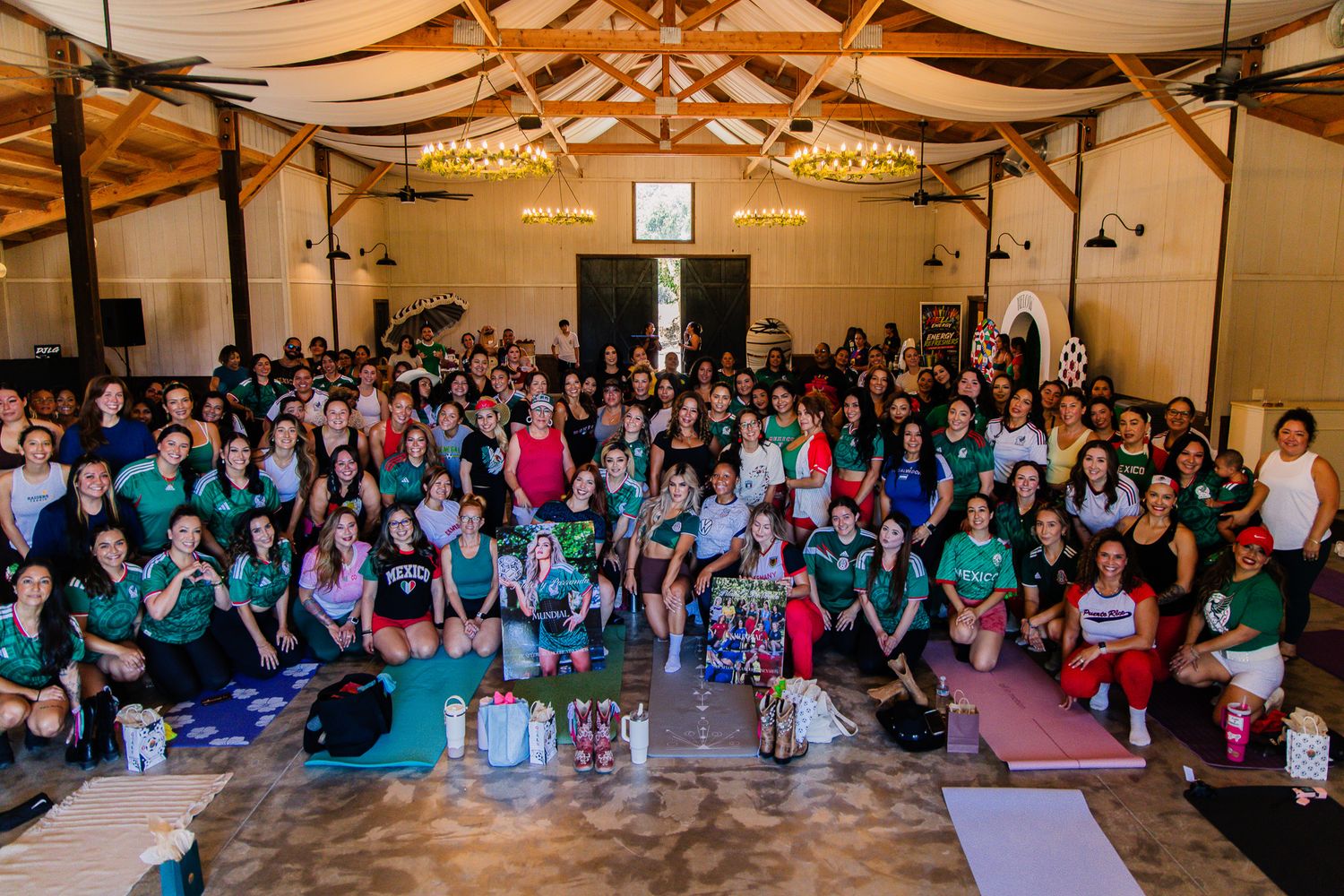 Large group of women posing together in a decorated wooden hall during a yoga retreat event.