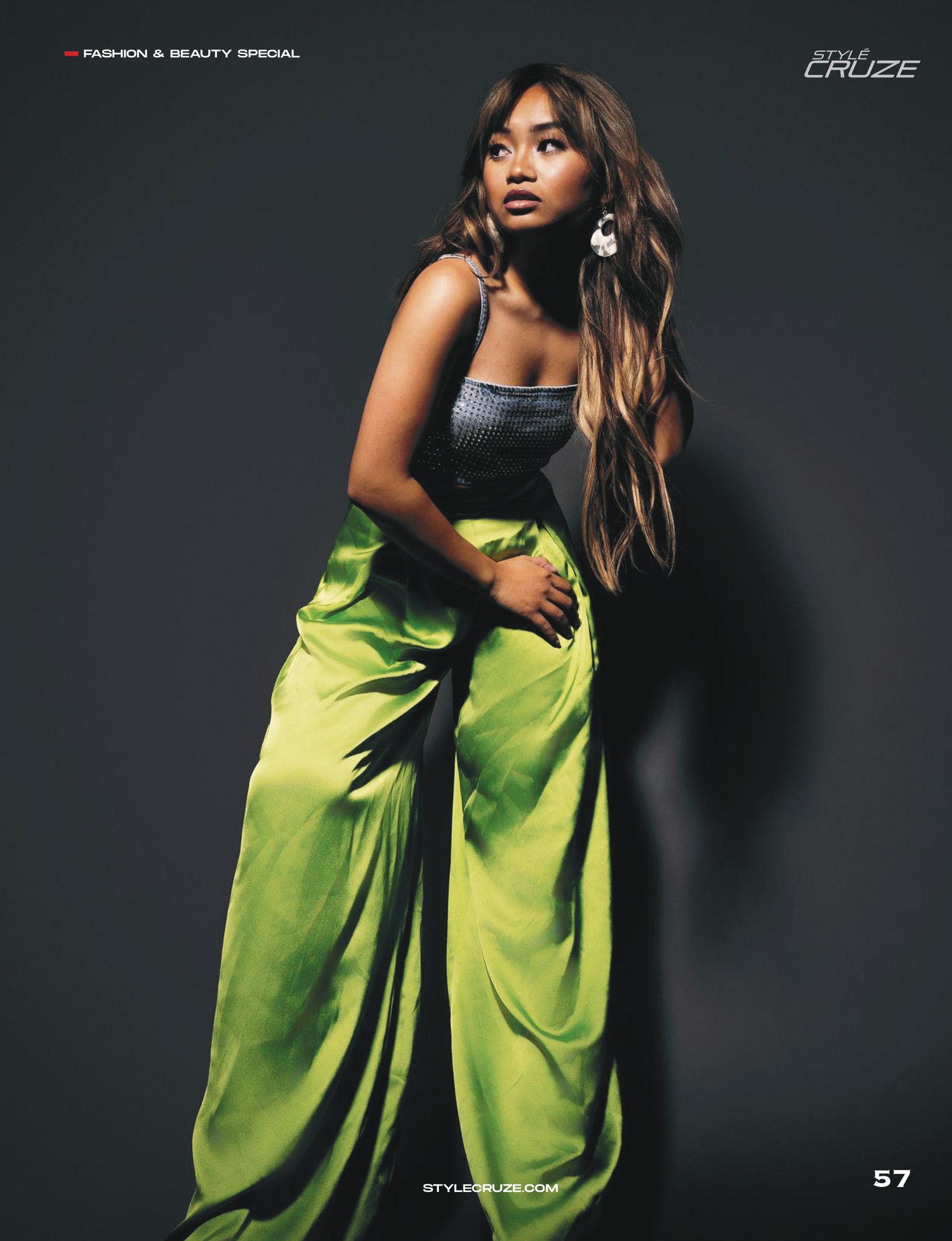 Fashion model poses in black top and lime green flowing pants against dark background in dramatic editorial shot.