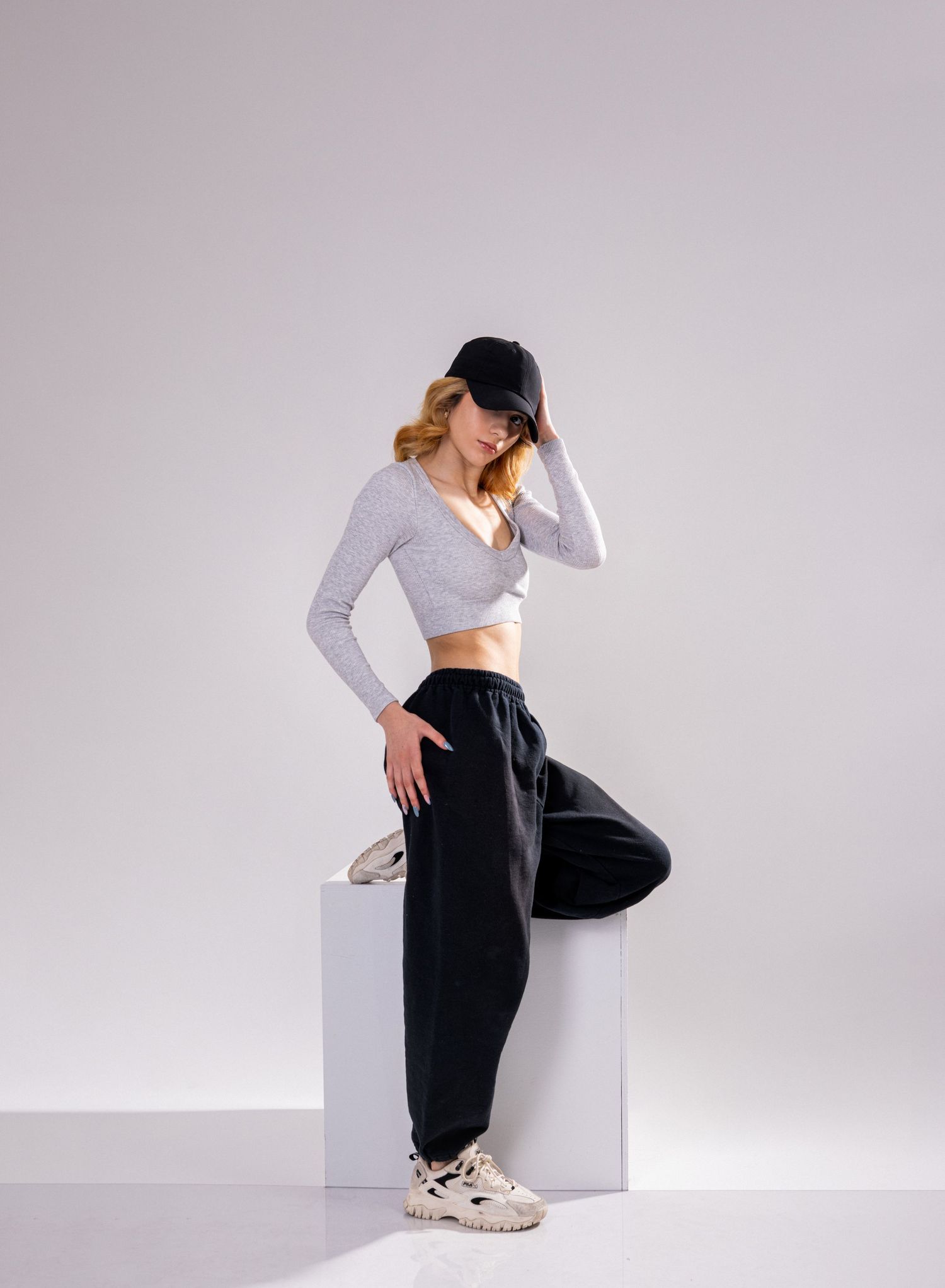 A person in black pants and white long-sleeved crop top strikes artistic poses against a minimalist gray backdrop.