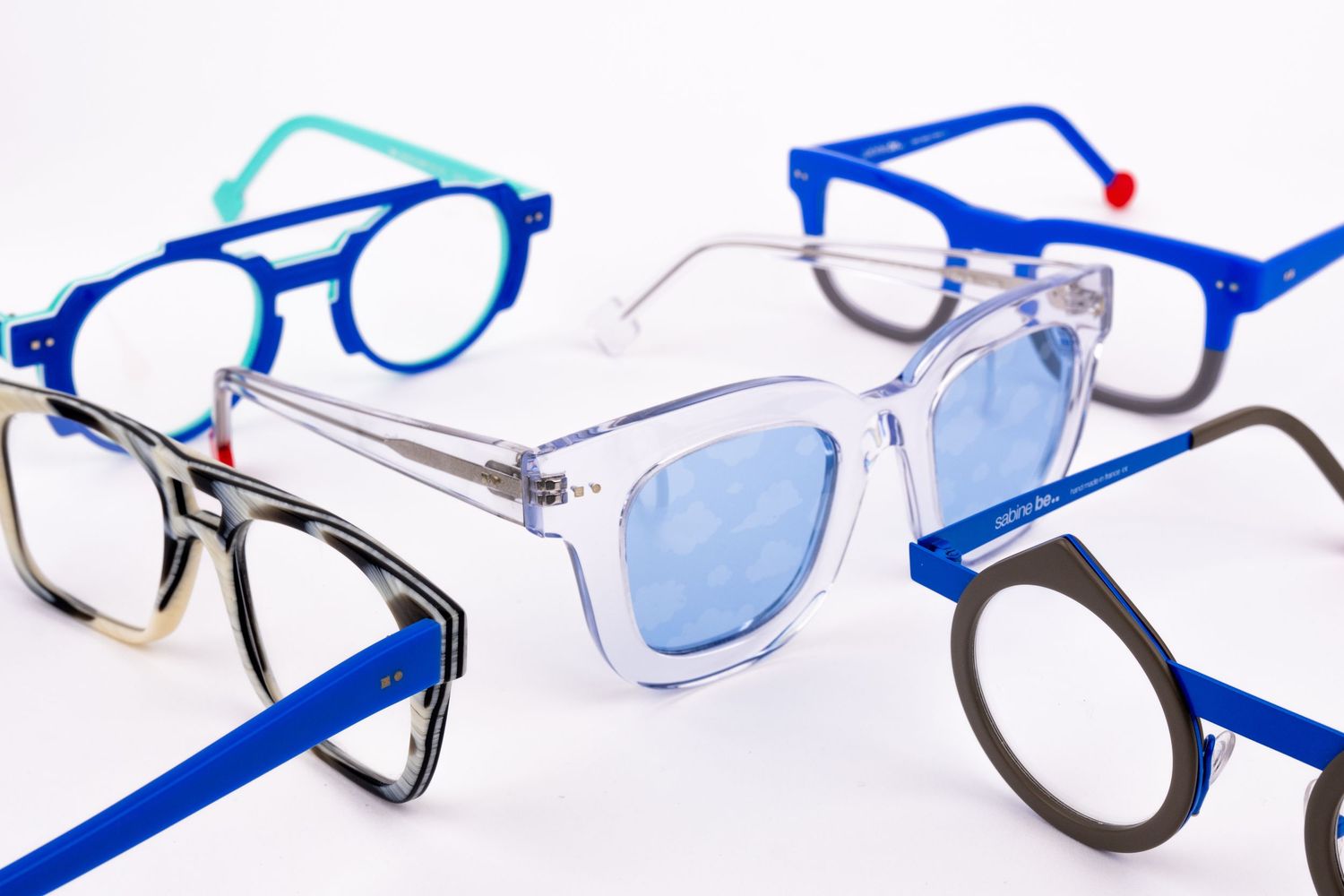 A row of eyeglasses and frames in various styles and colors laid out on a white surface for display.