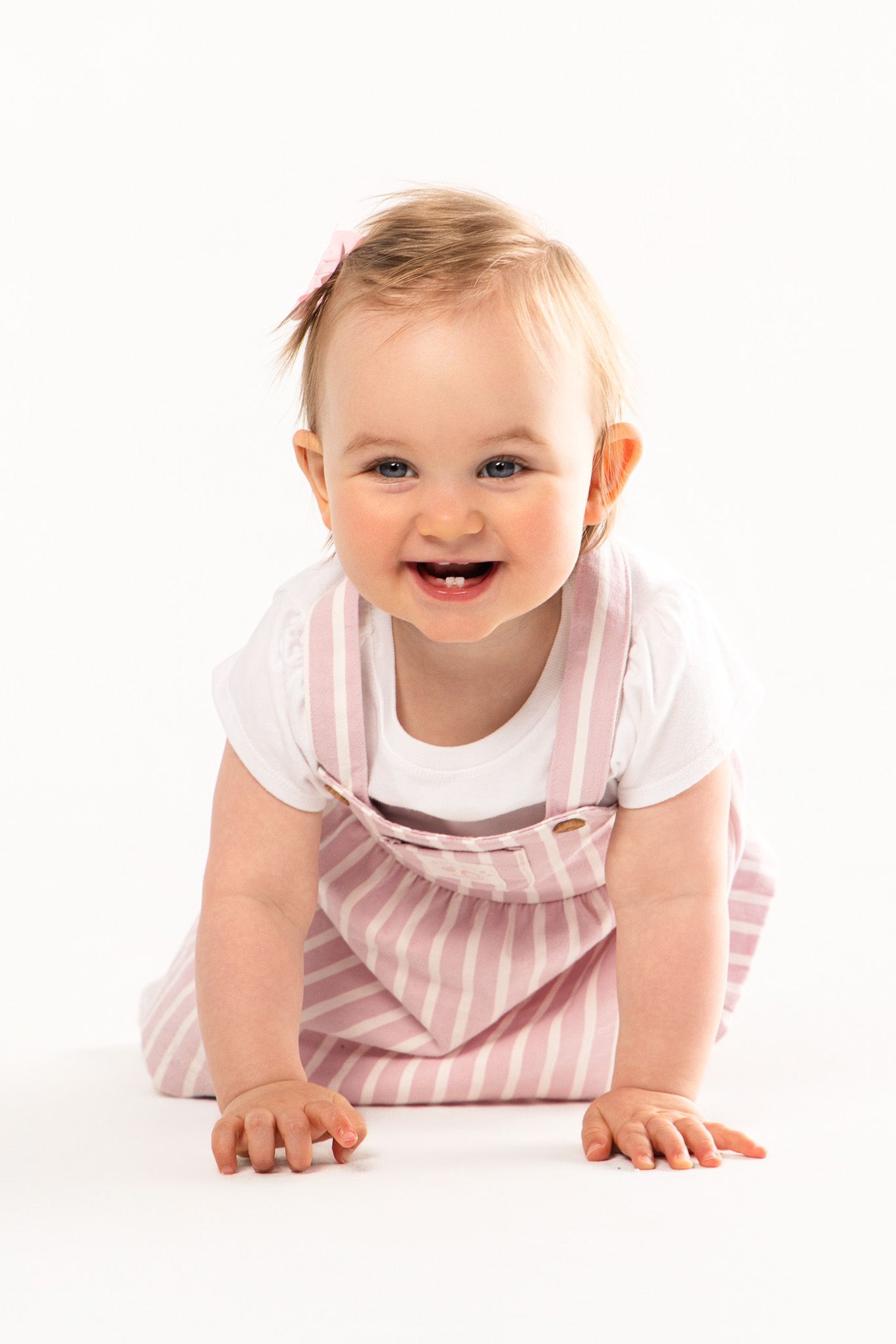 Happy baby in pink and white striped outfit crawling on white background.