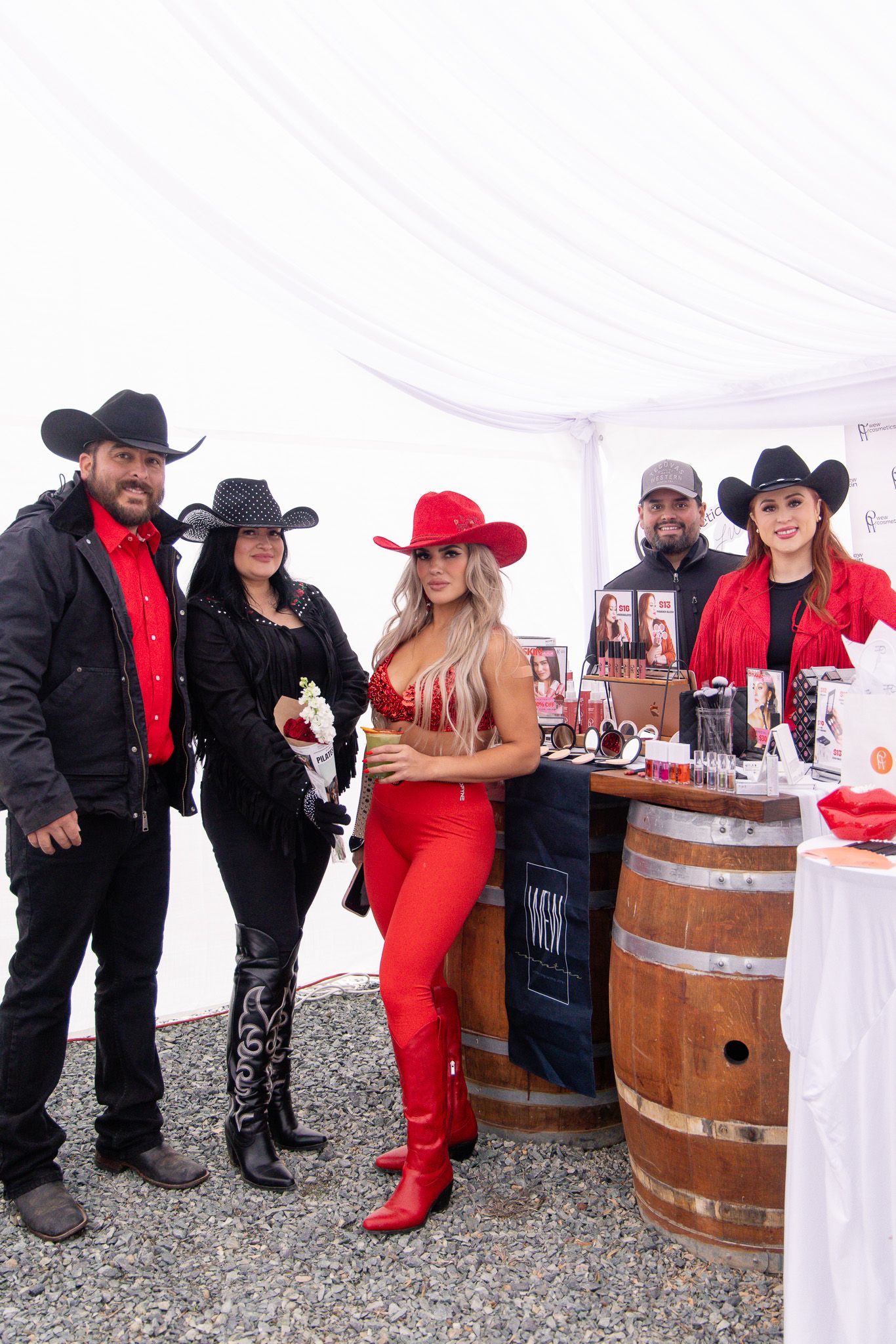 Group gathered at a western-themed event with wooden barrels and red and black outfits.