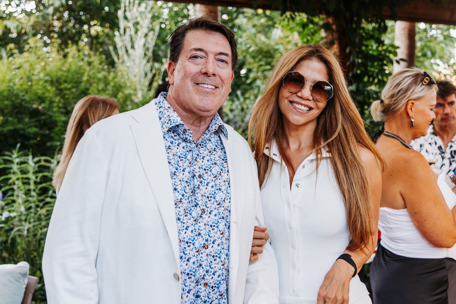 A group of people enjoying an outdoor gathering wearing white and floral clothing on a sunny day.