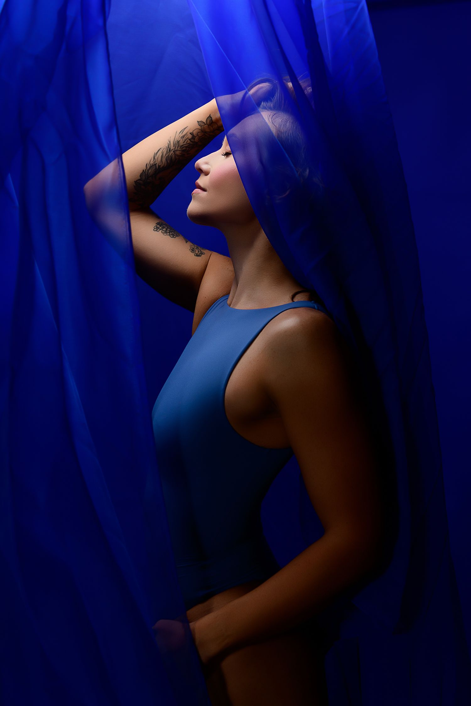 Artistic portrait against deep blue fabric backdrop with dramatic lighting and shadows in moody fashion photography style.