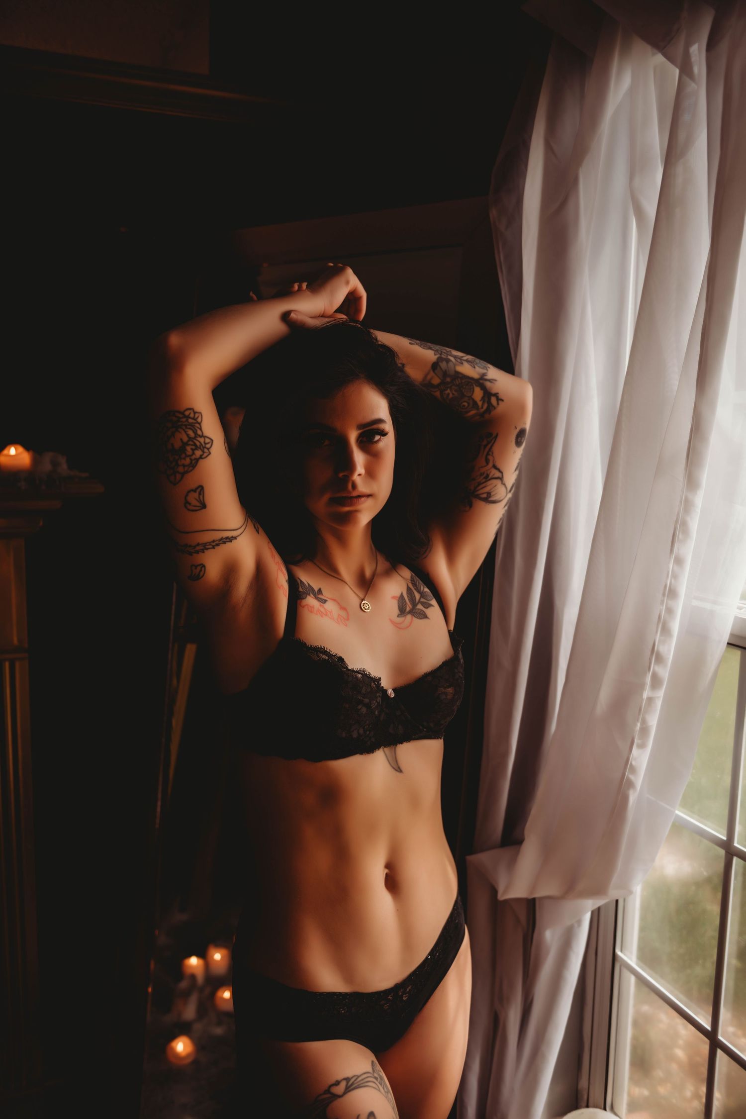 Artistic portrait session by window with sheer curtains and candlelight.