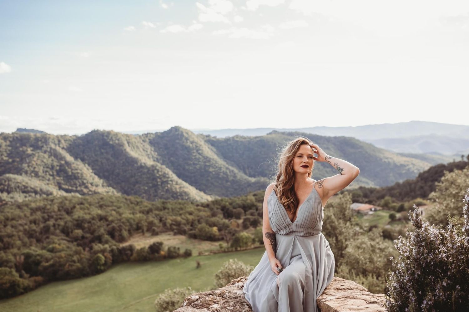 Sitting on a ledge in a beautiful mountainous landscape in a grey dress.