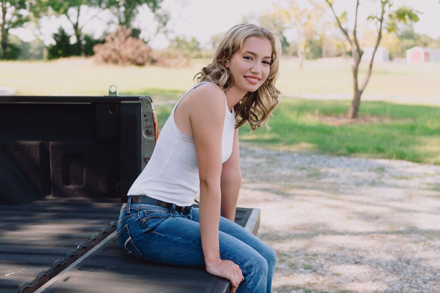 Casual portrait sitting on pickup truck bed in countryside setting.