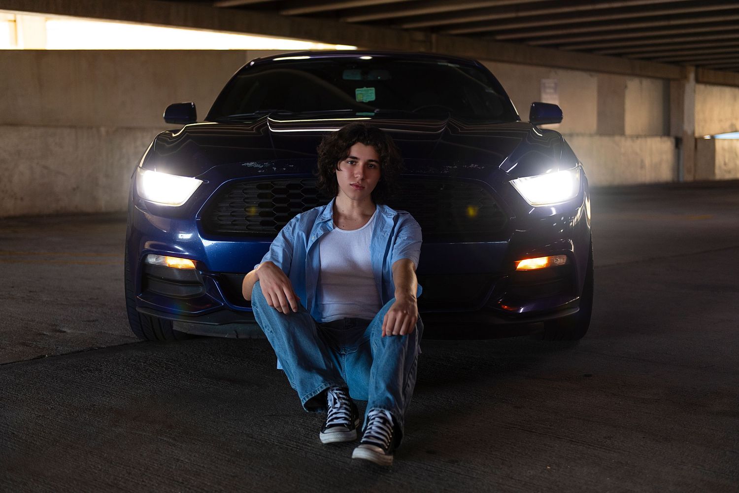 A person in casual clothing sits in various poses against a dark parking garage backdrop with cars visible.