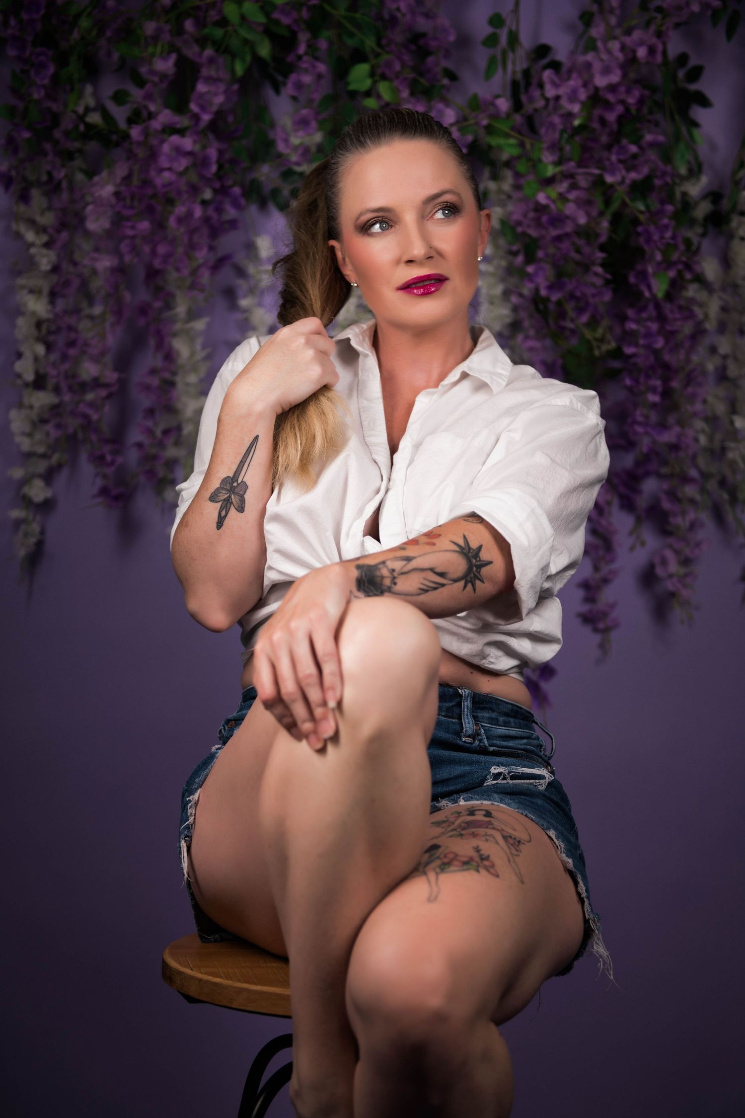 Boudoir photoshoot with white shirt and denim against purple floral backdrop.