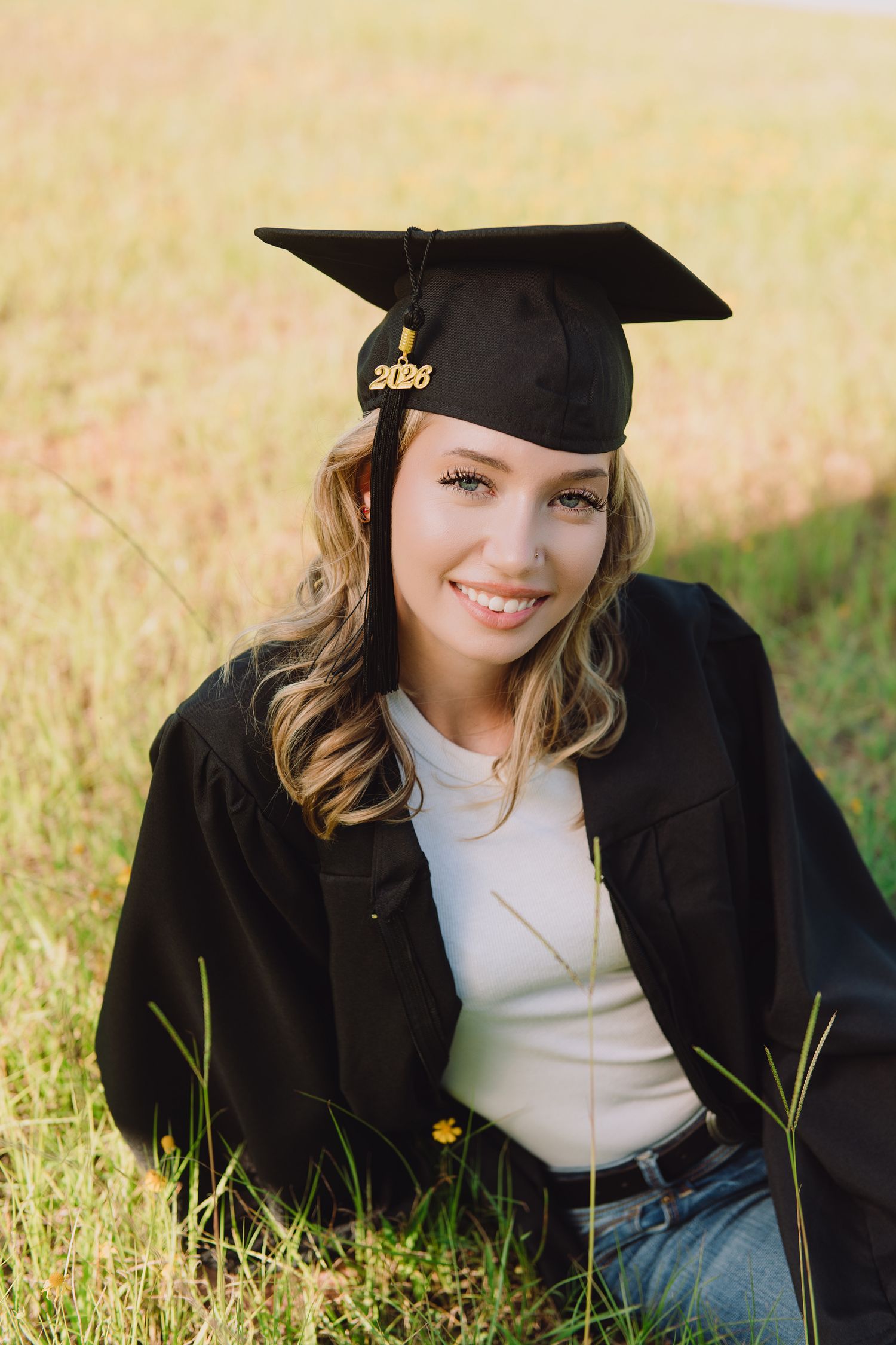 Graduation portraits taken outdoors in a sunny field with a graduate wearing traditional cap and gown lying in grass.