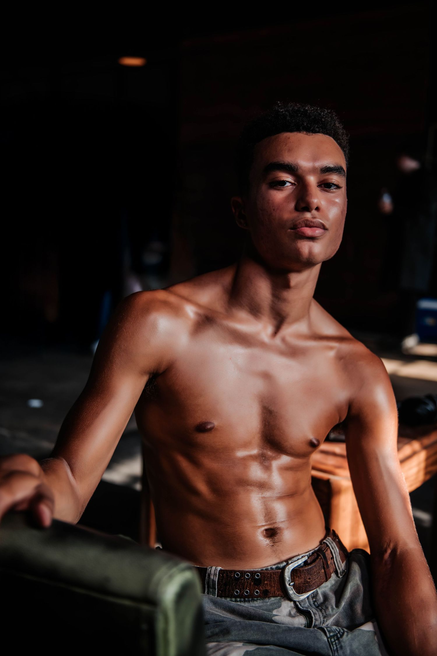 Dramatic low-light portrait showcasing athletic physique in casual setting.