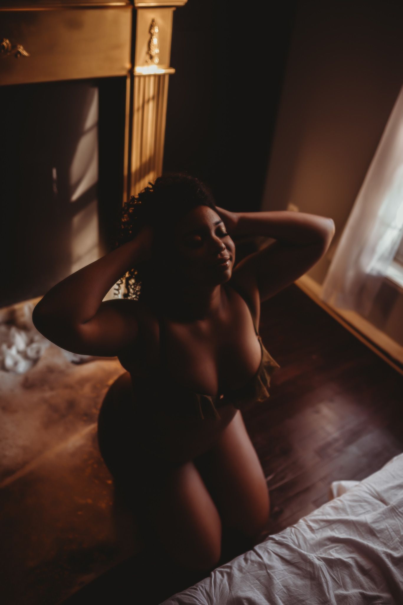 Silhouetted figure near window in moody indoor lighting creates artistic composition.