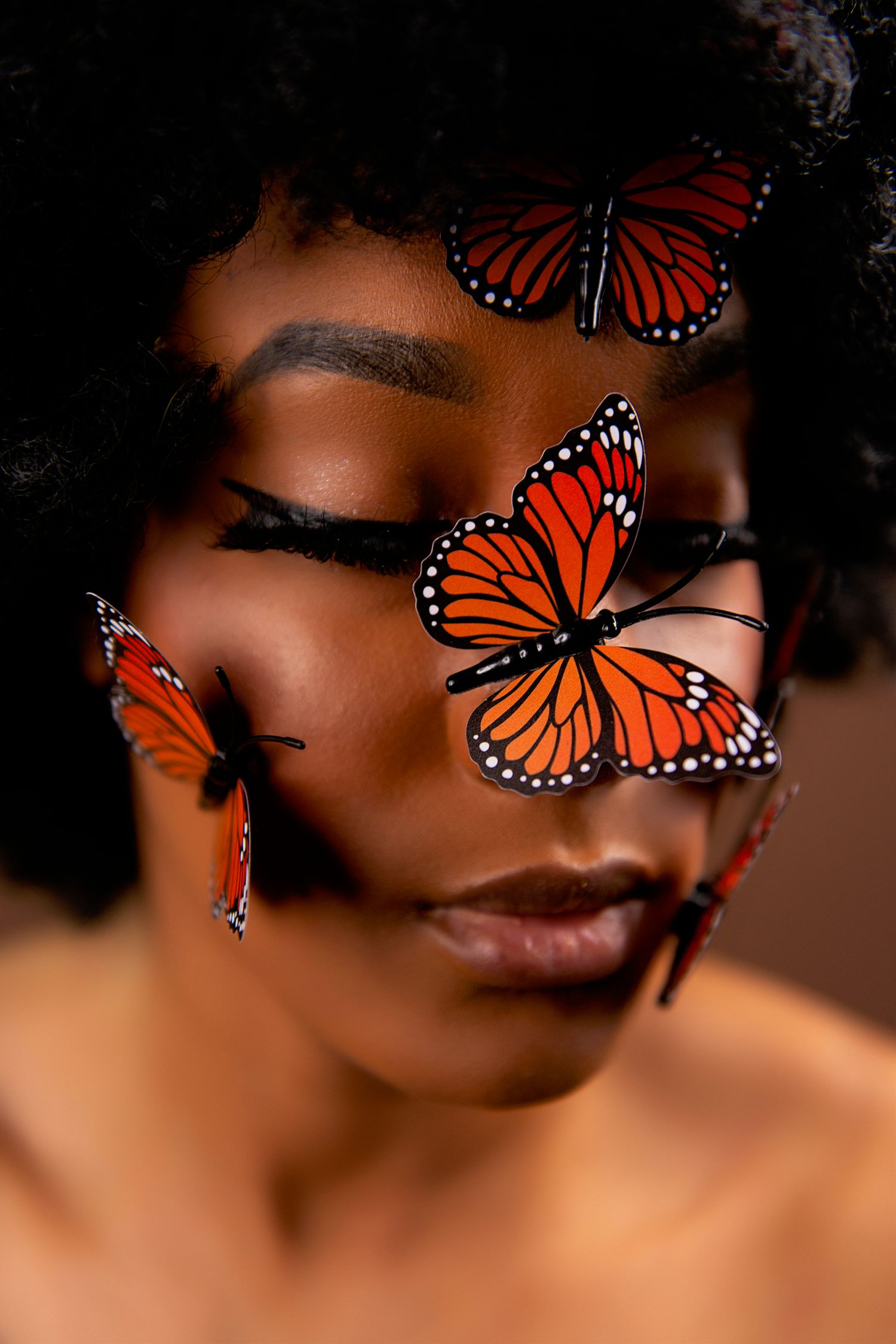 Close-up portrait of a woman with monarch butterflies resting on her face against a dark background.