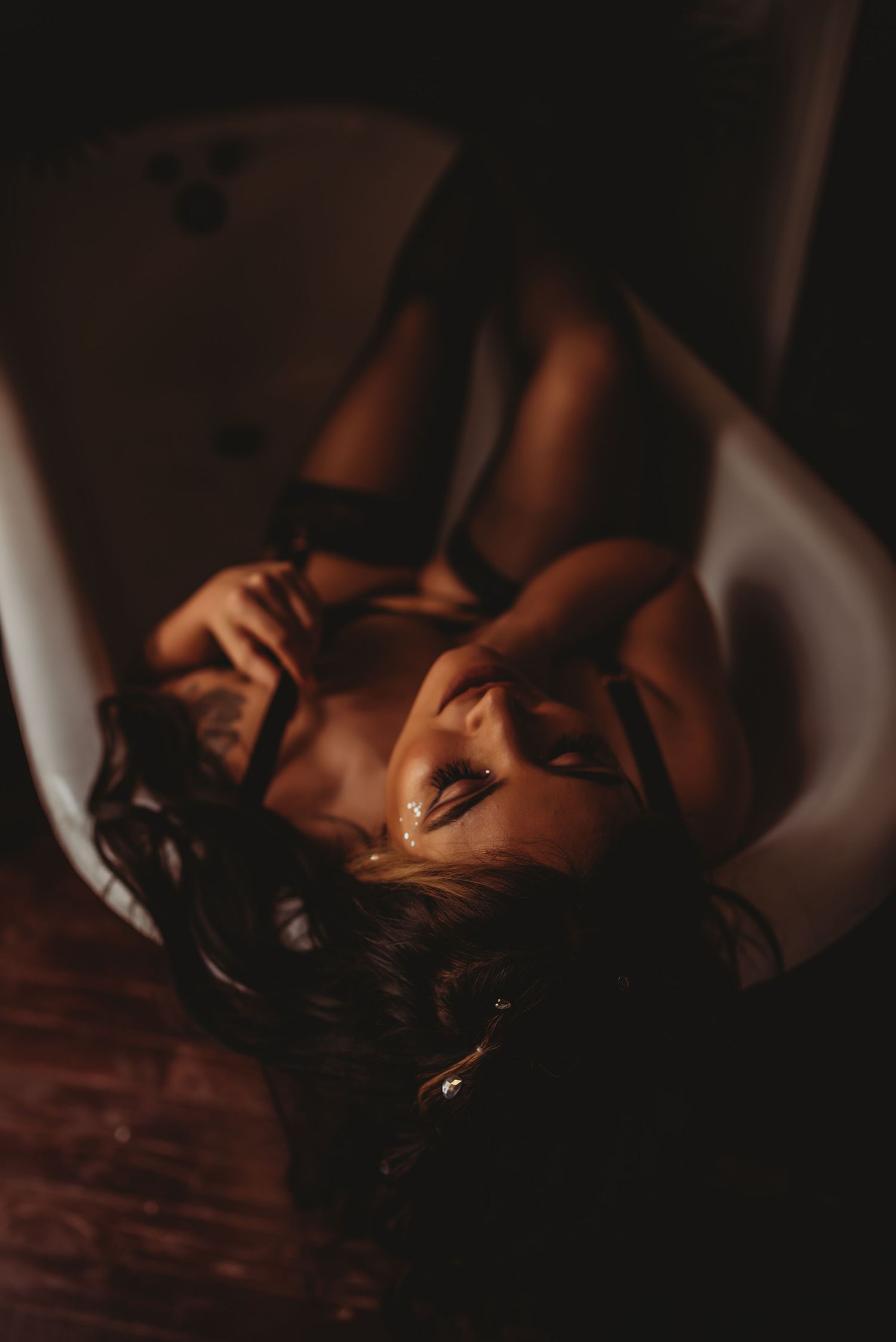 A woman rests on a dark wooden floor in a moody, dimly lit room creating a dramatic and intimate atmosphere.