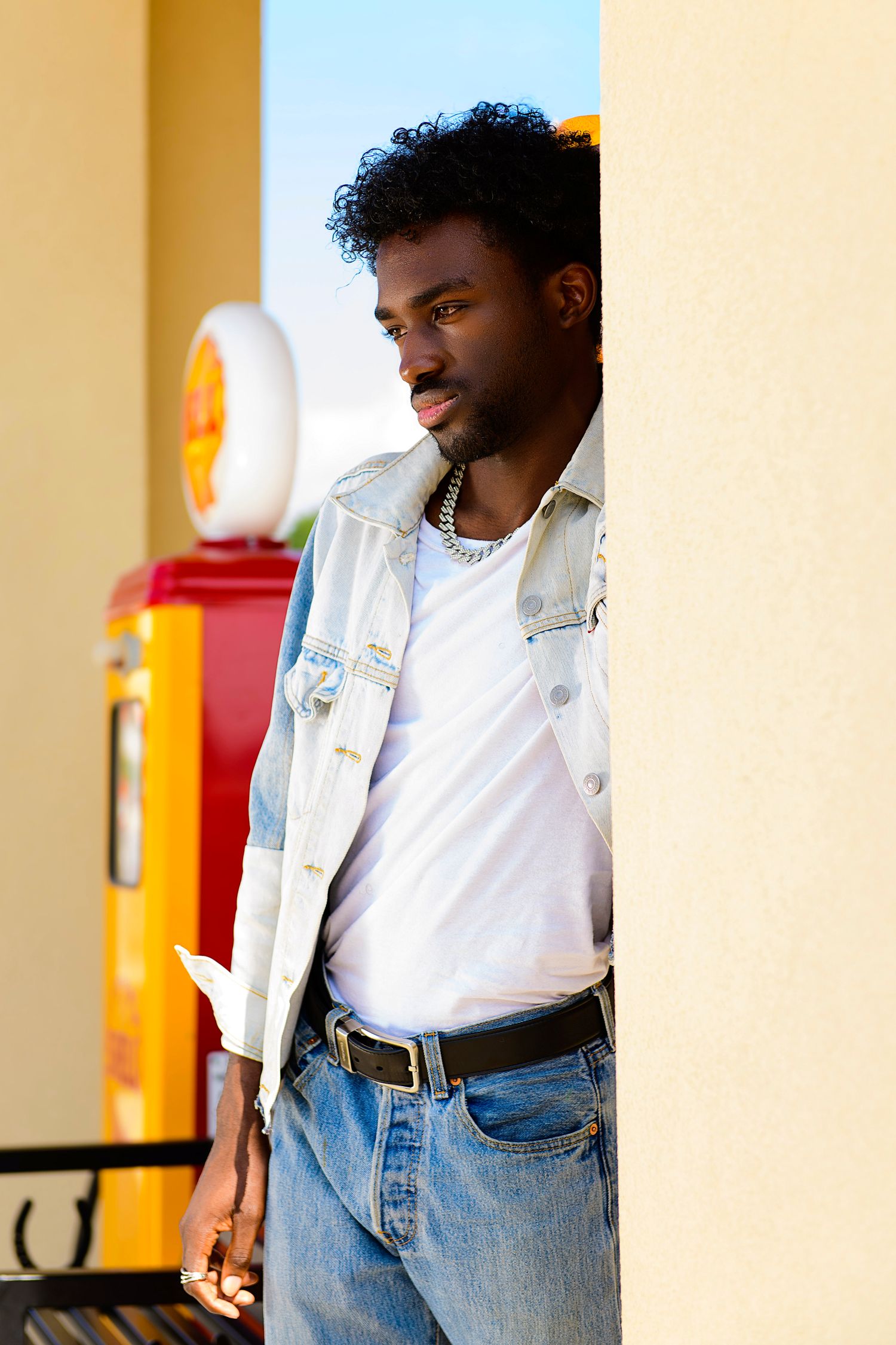 Person in white shirt and jeans poses against wall with orange accent and sunlight.