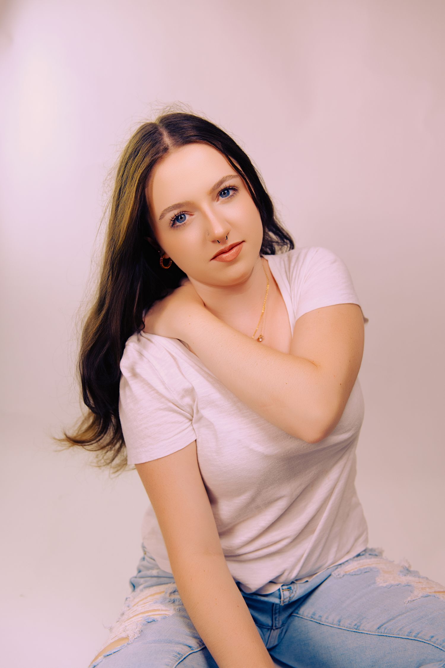 Studio portrait on pink backdrop with soft lighting and casual styling.