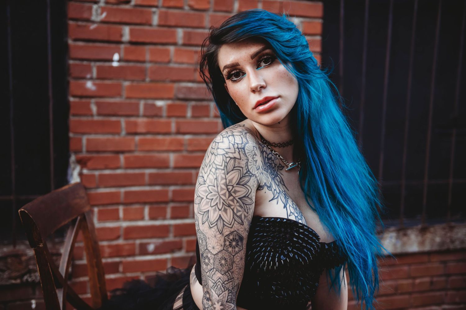 Alternative style portrait with vibrant blue hair against industrial brick backdrop.