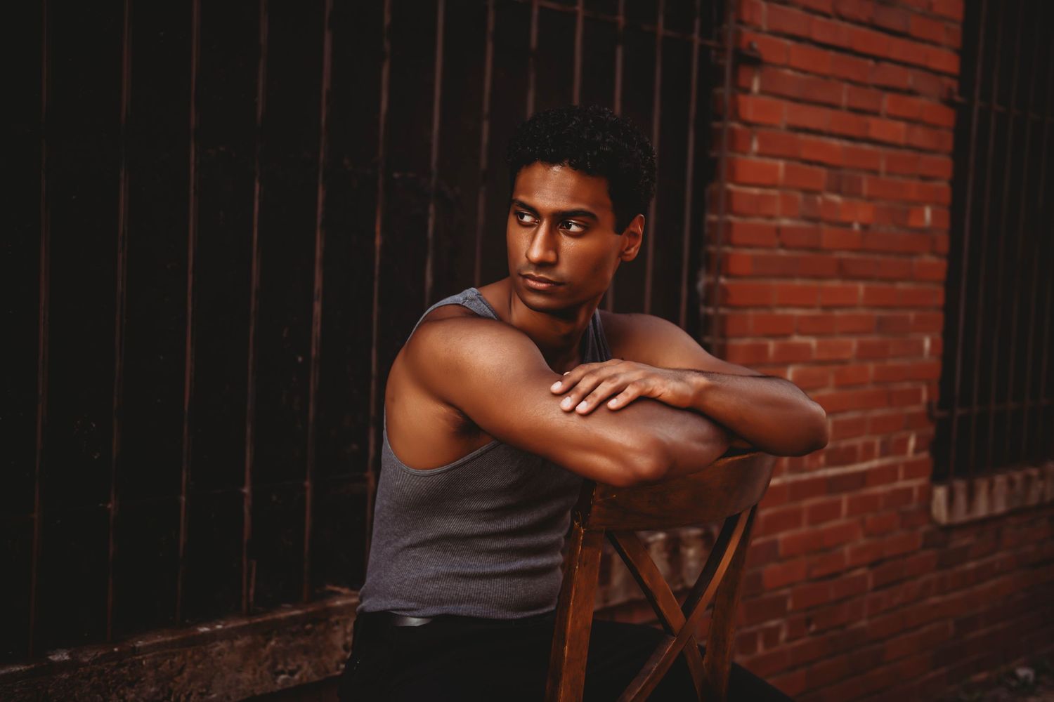 Artistic portrait against brick wall background with dramatic shadows and lighting.