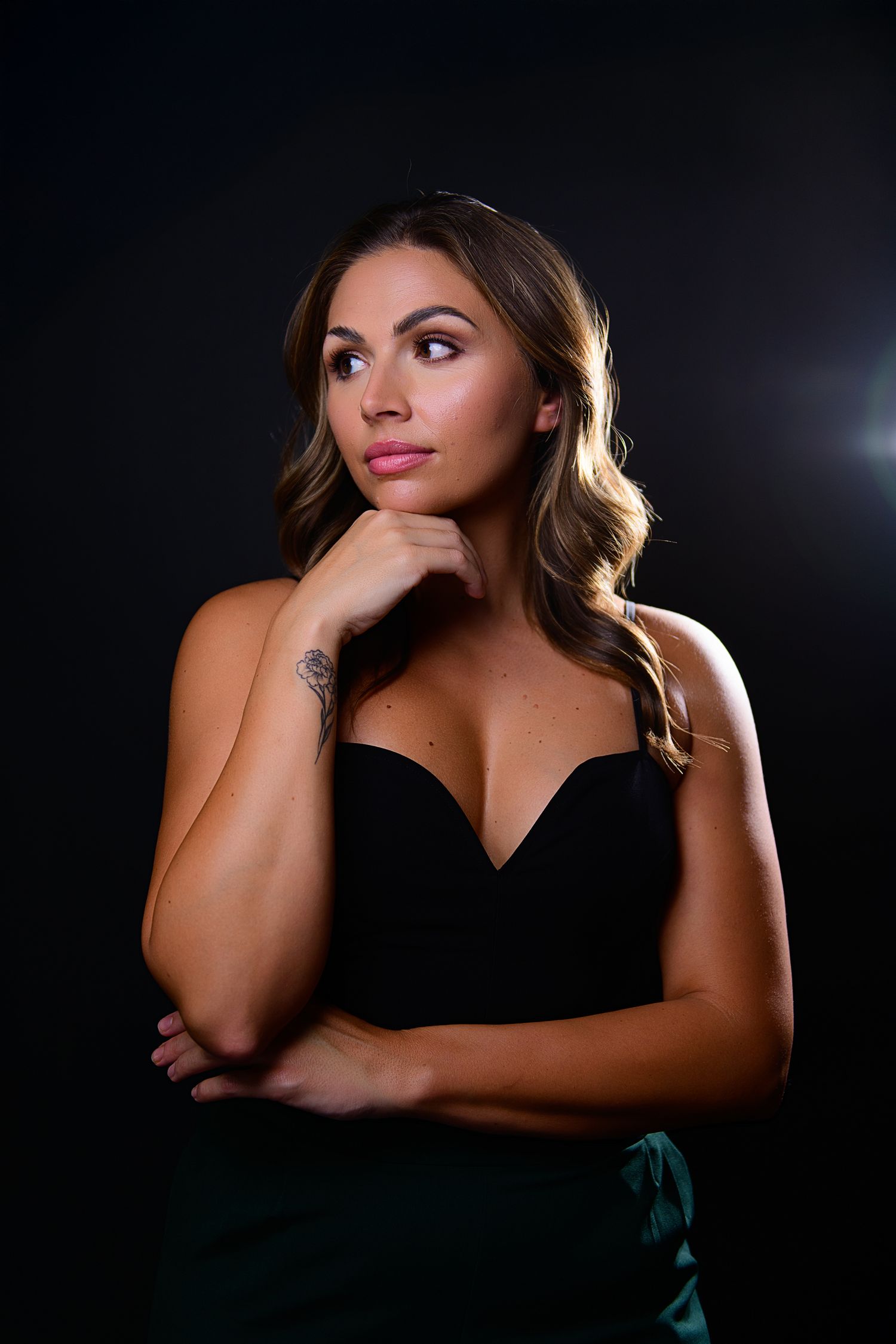 Studio portrait of someone in a black dress against dark background with dramatic lighting creating a moody atmosphere.