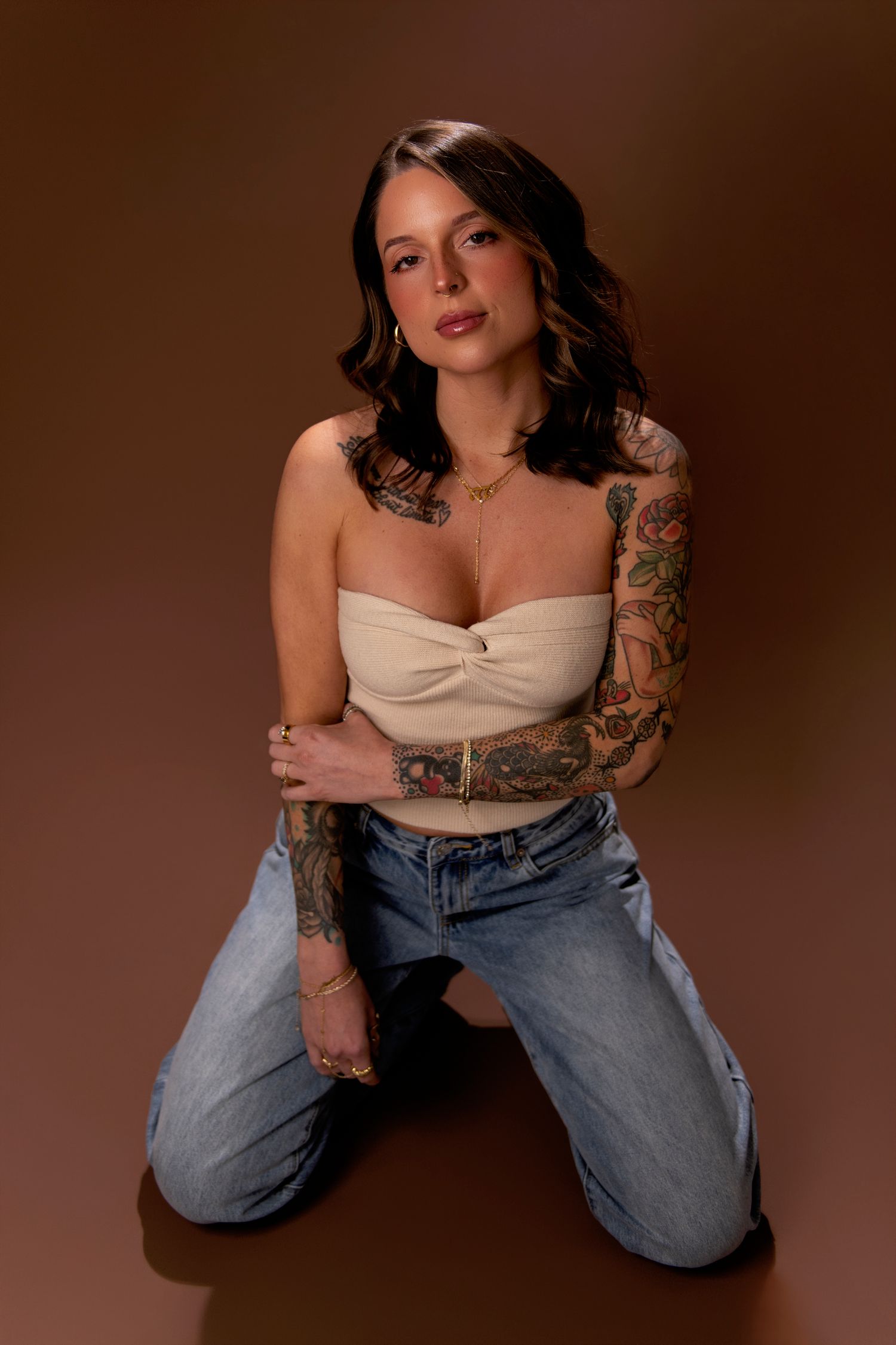 A person in a beige top and jeans poses against a brown backdrop in a series of artistic portrait shots.
