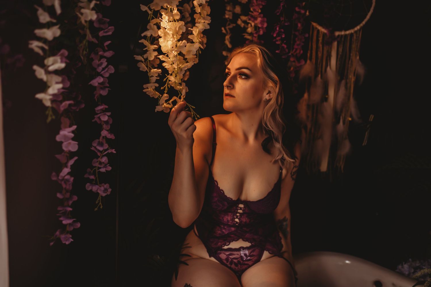 Person in purple lingerie poses against dark floral backdrop in moody boudoir photoshoot.