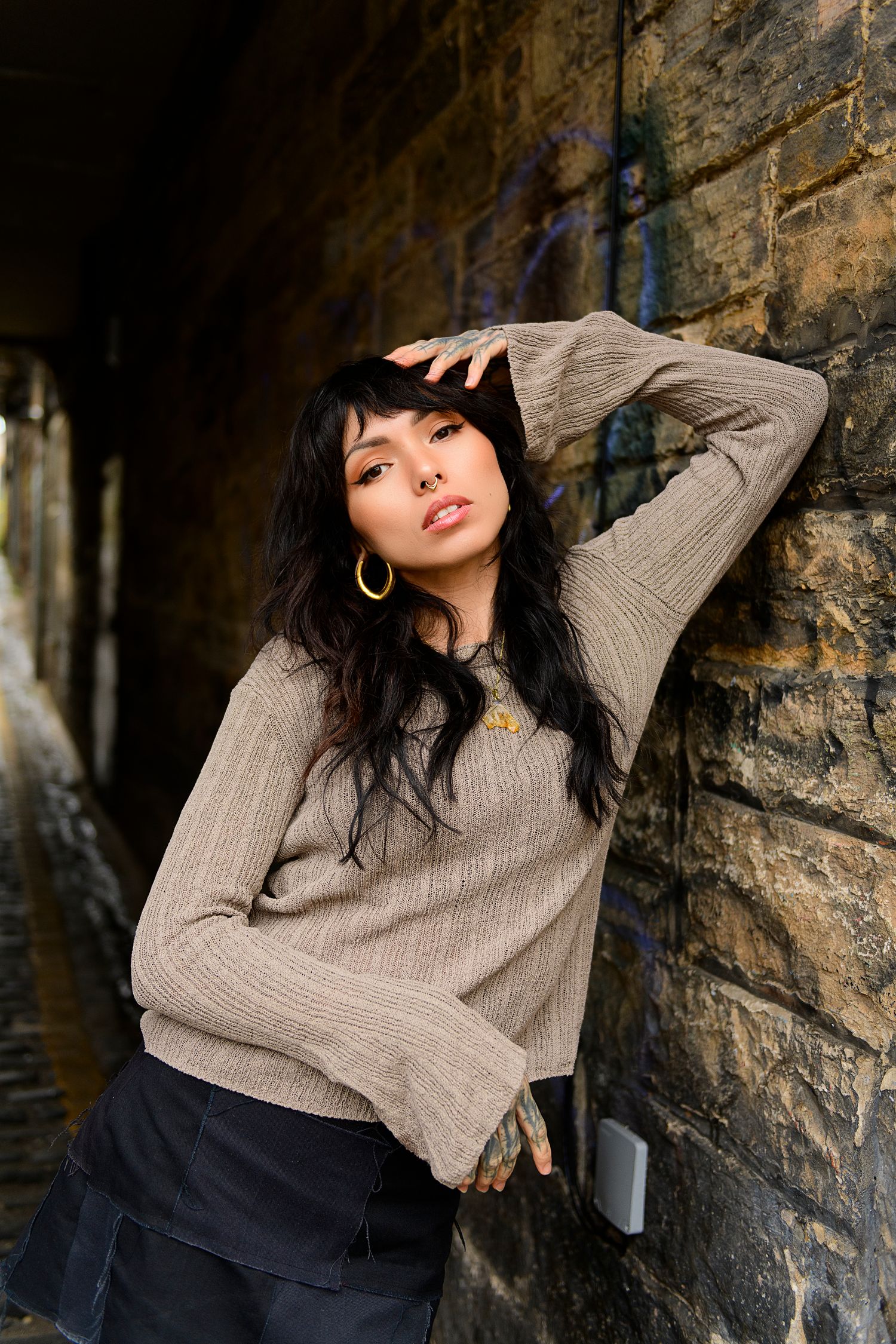 A model in a beige sweater poses dramatically against a stone wall in an artistic fashion photoshoot series.