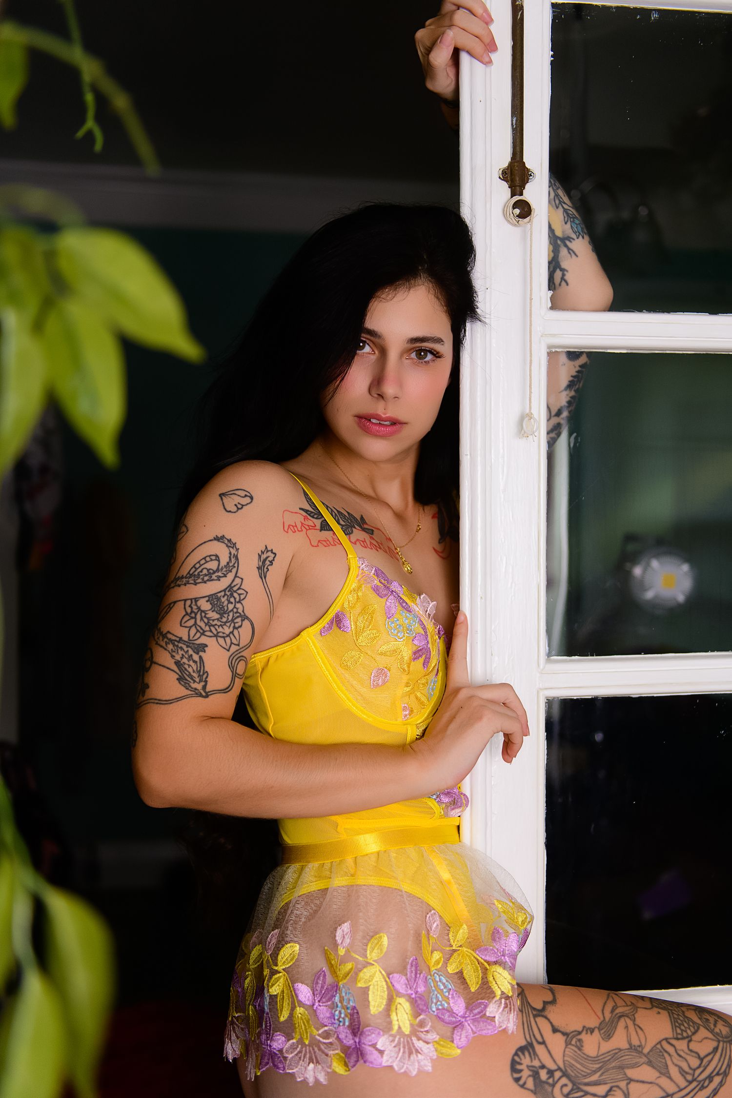 A floral yellow maternity photoshoot features multiple poses against white windows with green foliage in background.
