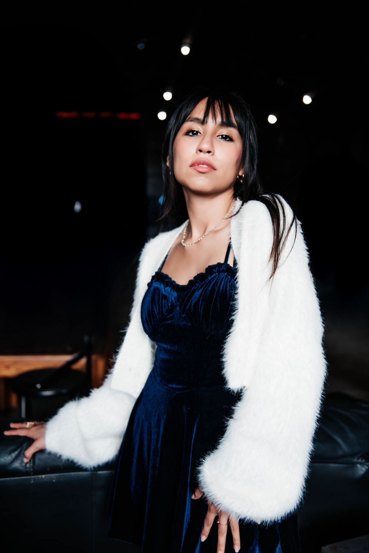 Elegant portrait featuring blue velvet dress and white fuzzy coat against dark background.