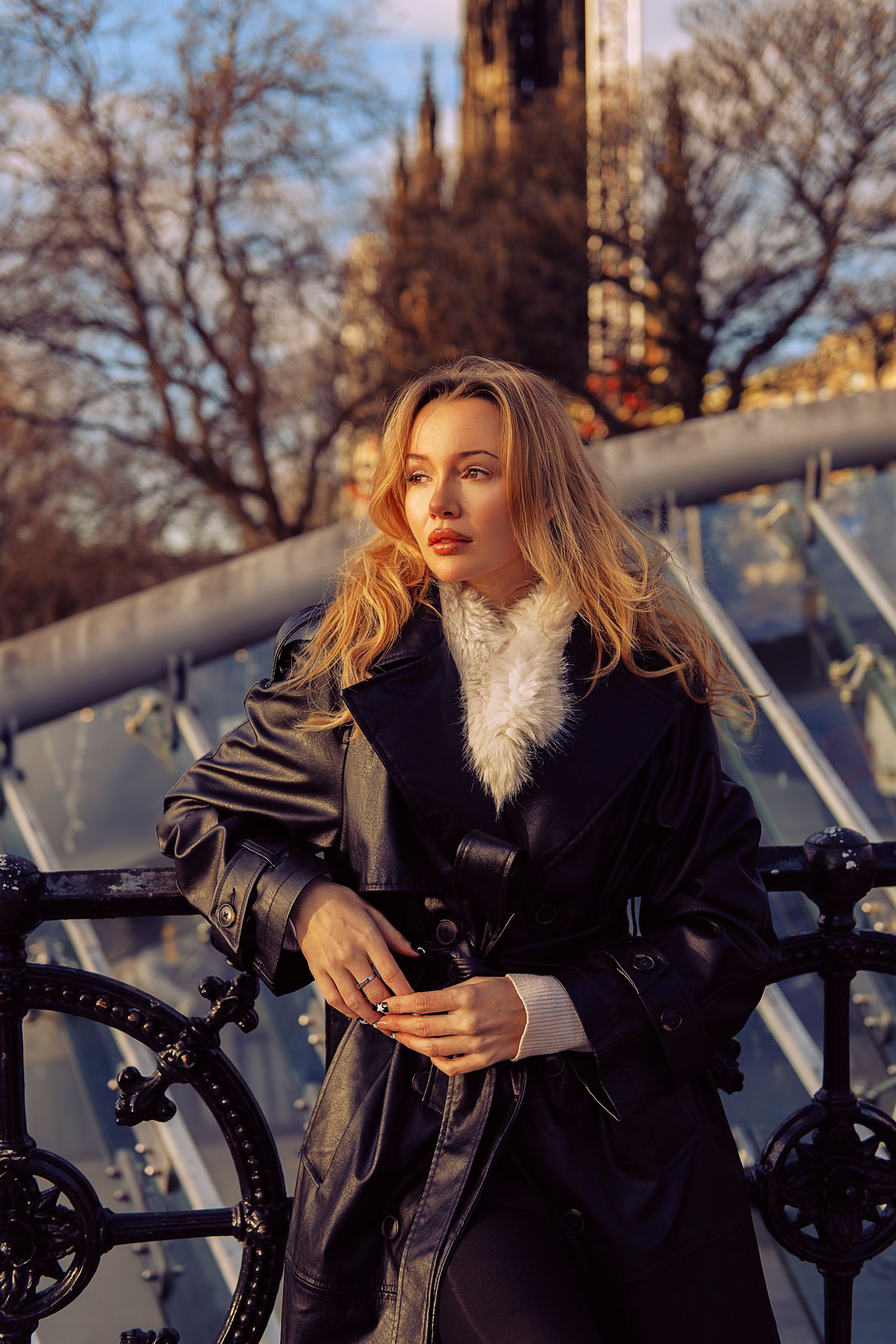 Fashion model in winter attire poses with motorcycle during golden hour photoshoot outdoors.