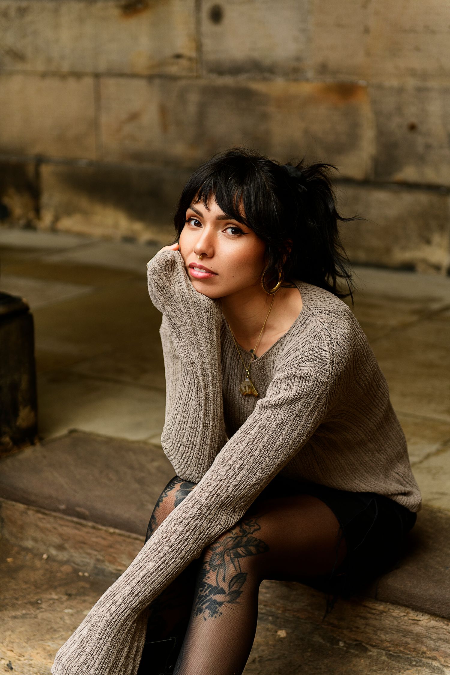 A series of moody portraits showing a person in a gray sweater with tattoos sitting against a rustic wooden backdrop.