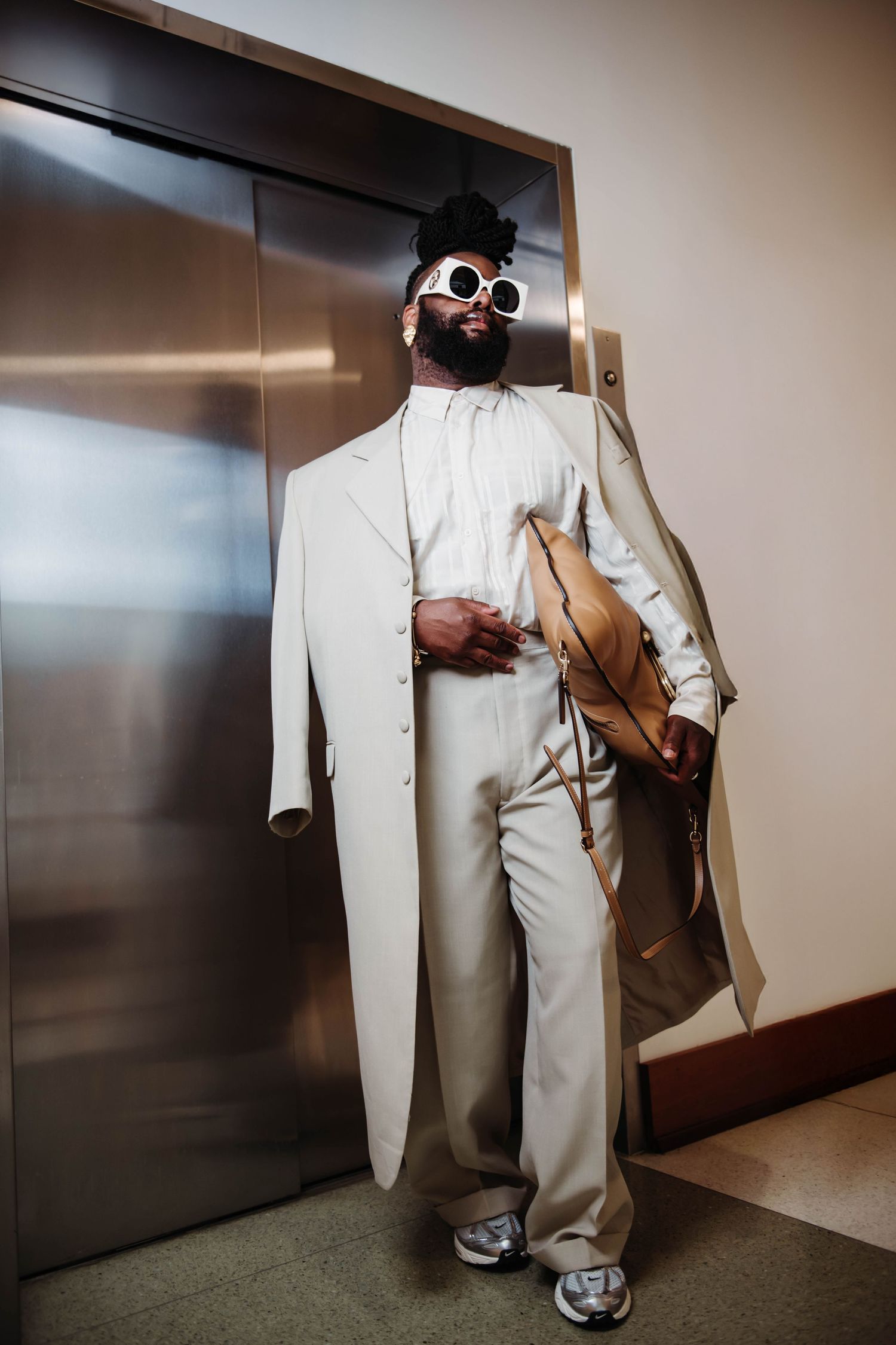 Person in white suit and sneakers photographed from waist down in modern hallway.
