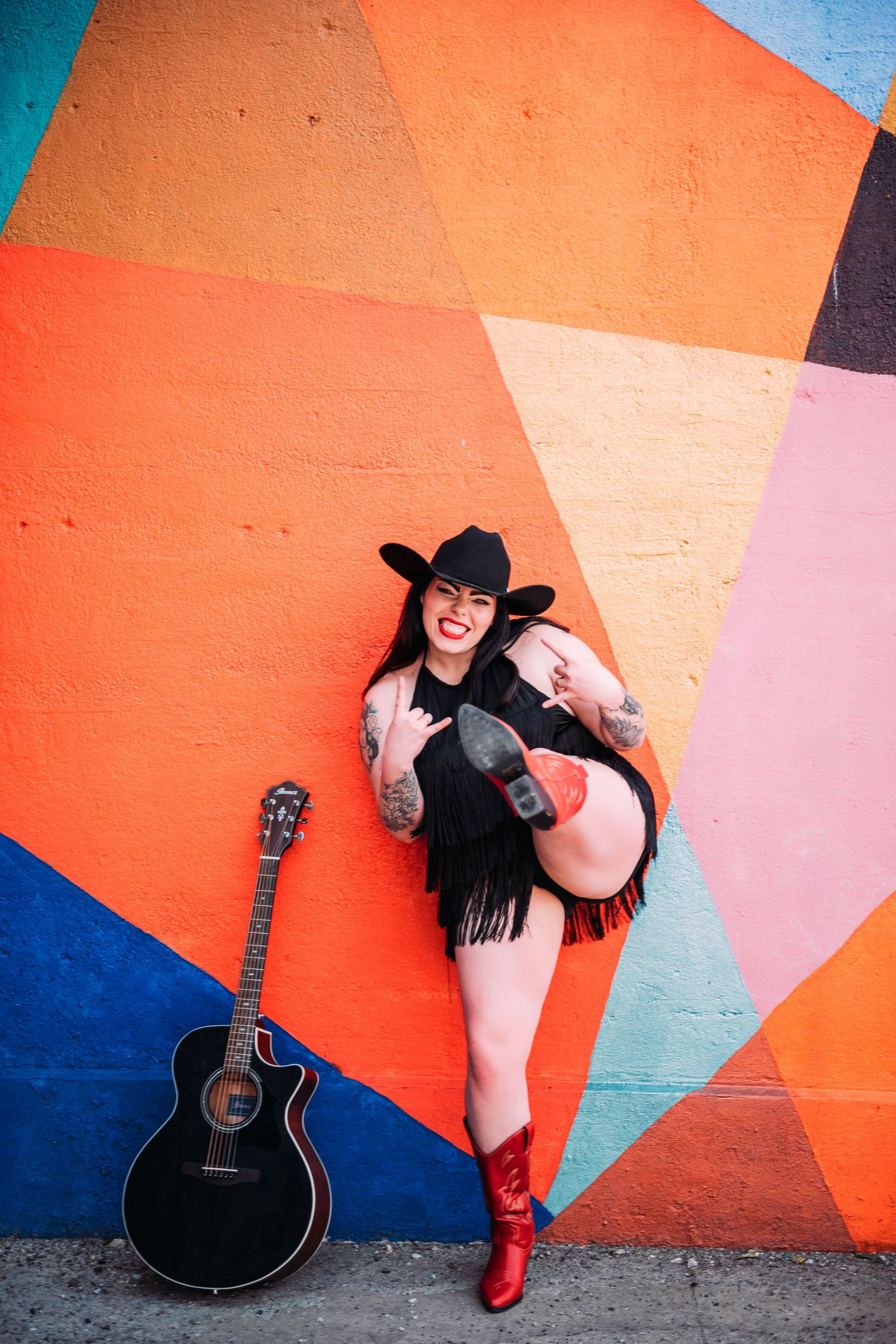 Colorful portrait session with acoustic guitar against geometric painted wall mural.